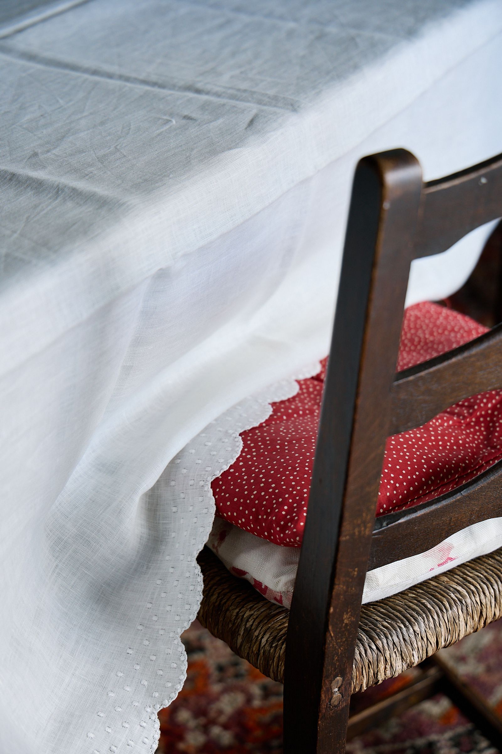 Italian linen tablecloth spills over wooden rush chair and red cushion