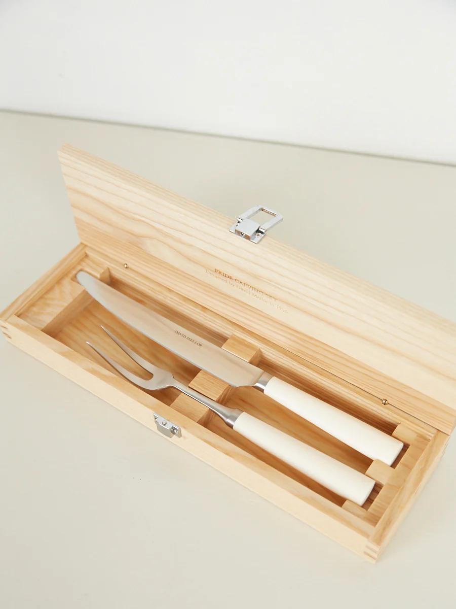 Wooden box with carving set. White-handled utensils in slots. Open lid shows Belgian Linen lining.