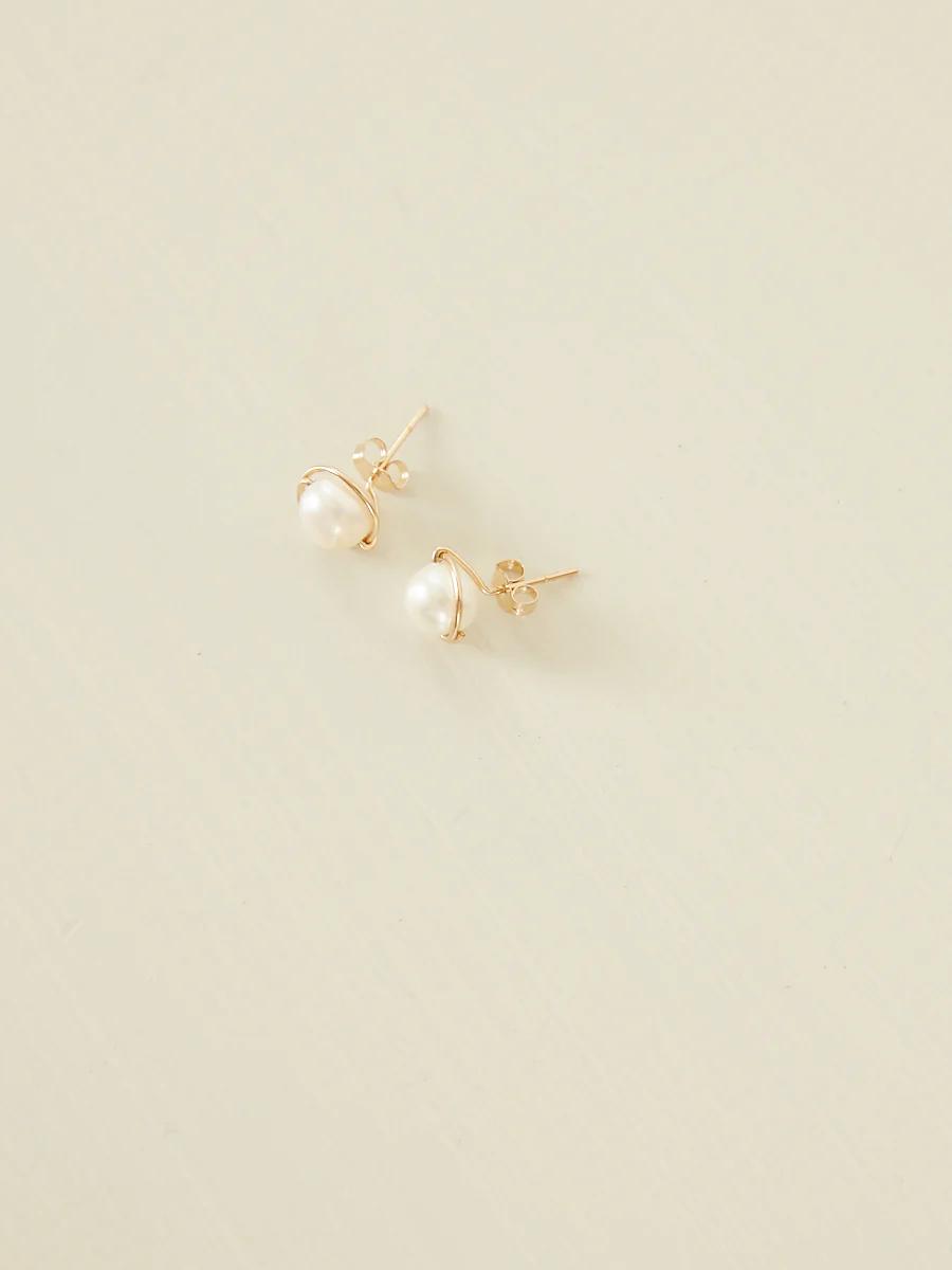 Gold pearl stud earrings on light surface. White pearl in intricate gold setting.