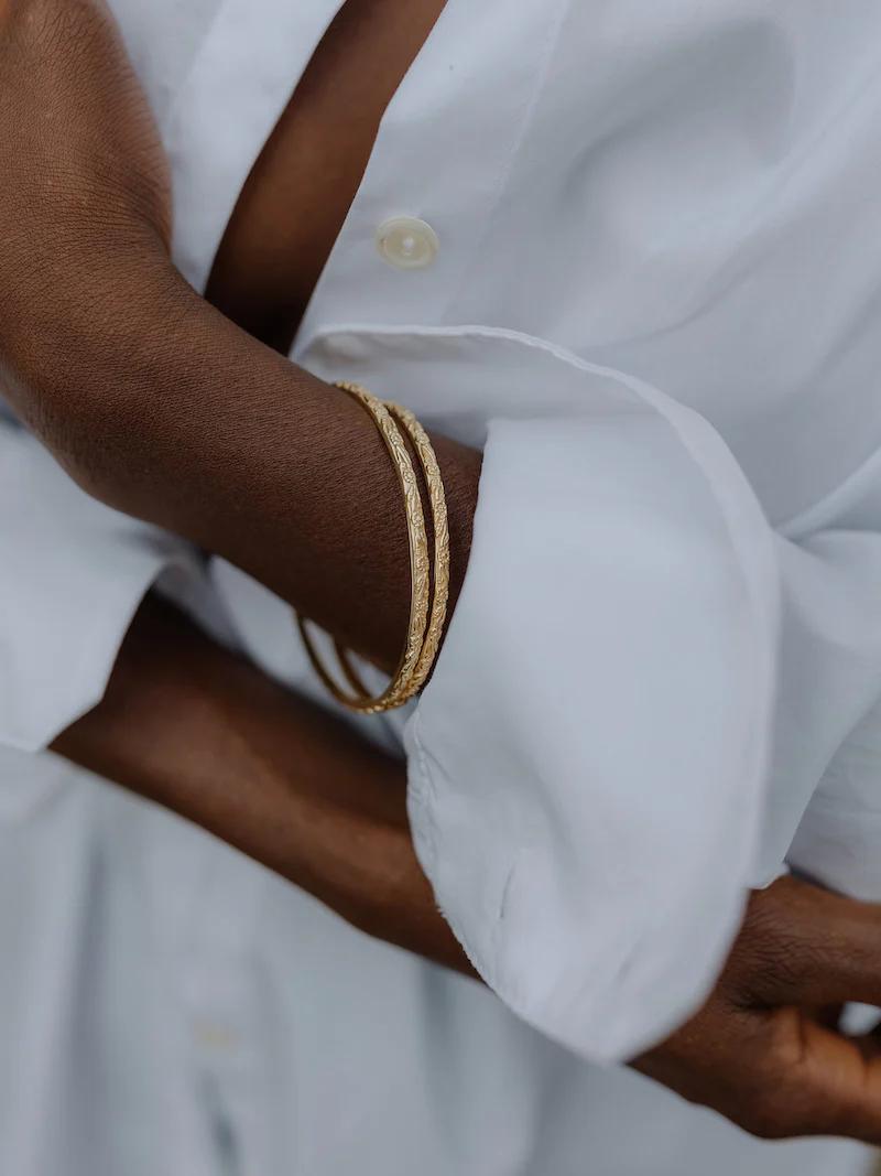 Crossed arms in white long-sleeve shirt with unbuttoned cuffs. Two gold bangles on one wrist.