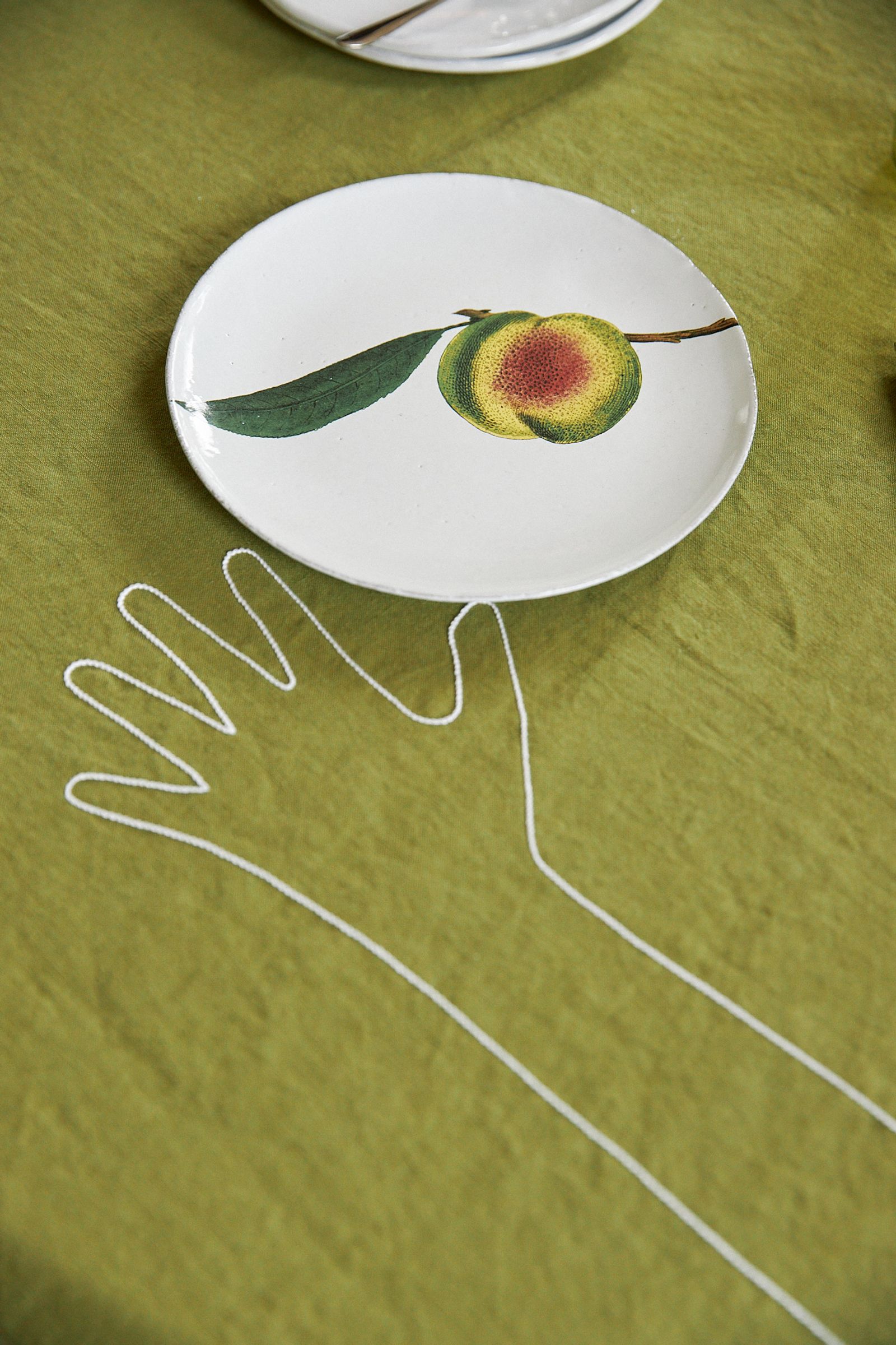 green tablecloth with embroidered hand stretched over the table to a plate