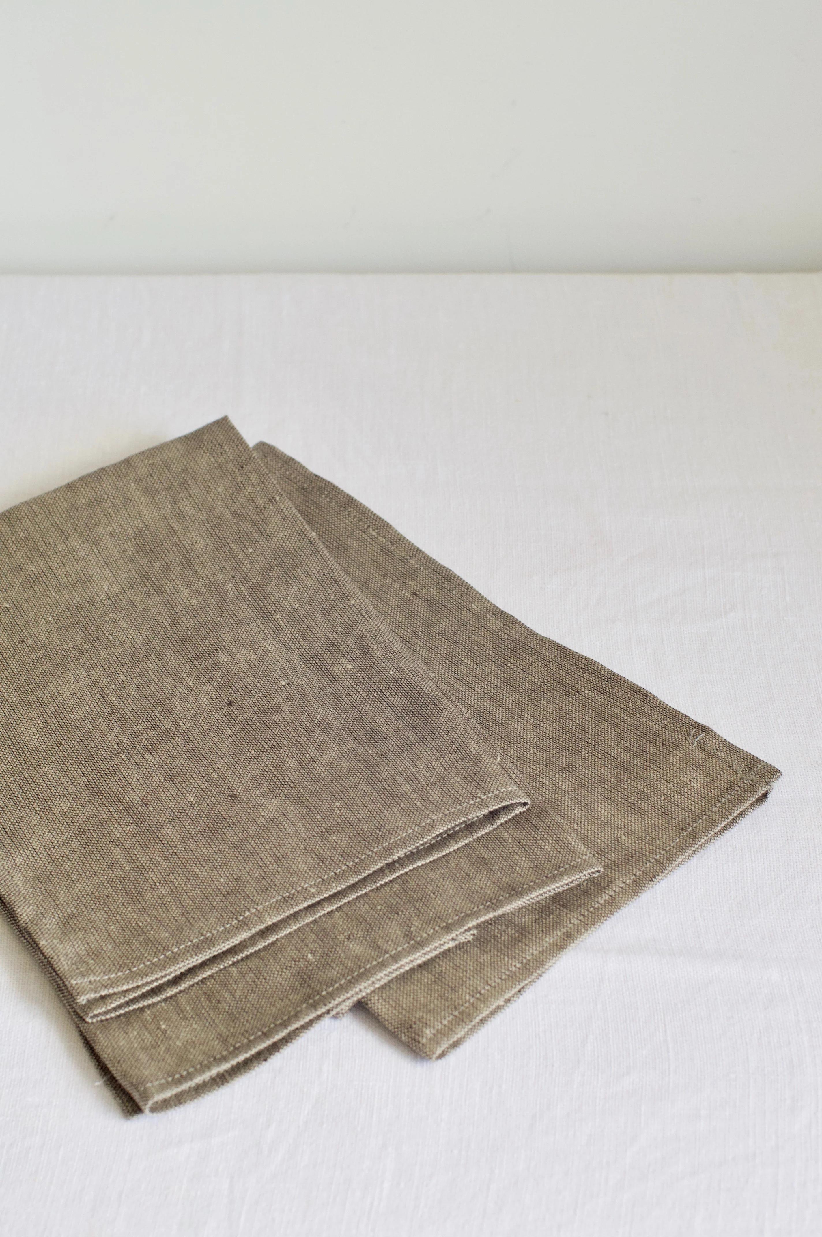 Neatly folded brown linen napkins on white surface. Textured fabric visible. Simple, elegant contemporary design.