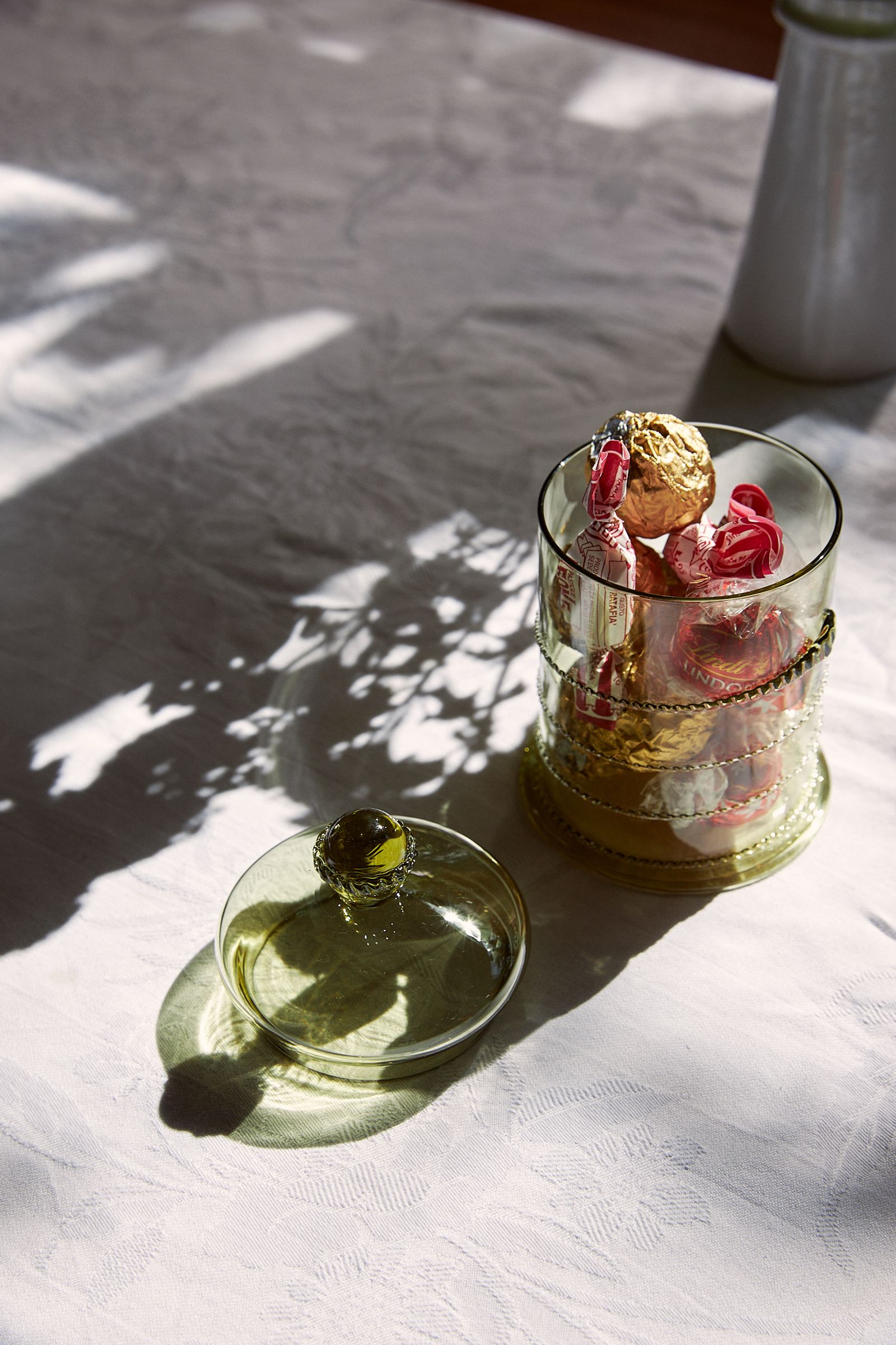 green glass jar sits with lid off on a table with white linen 