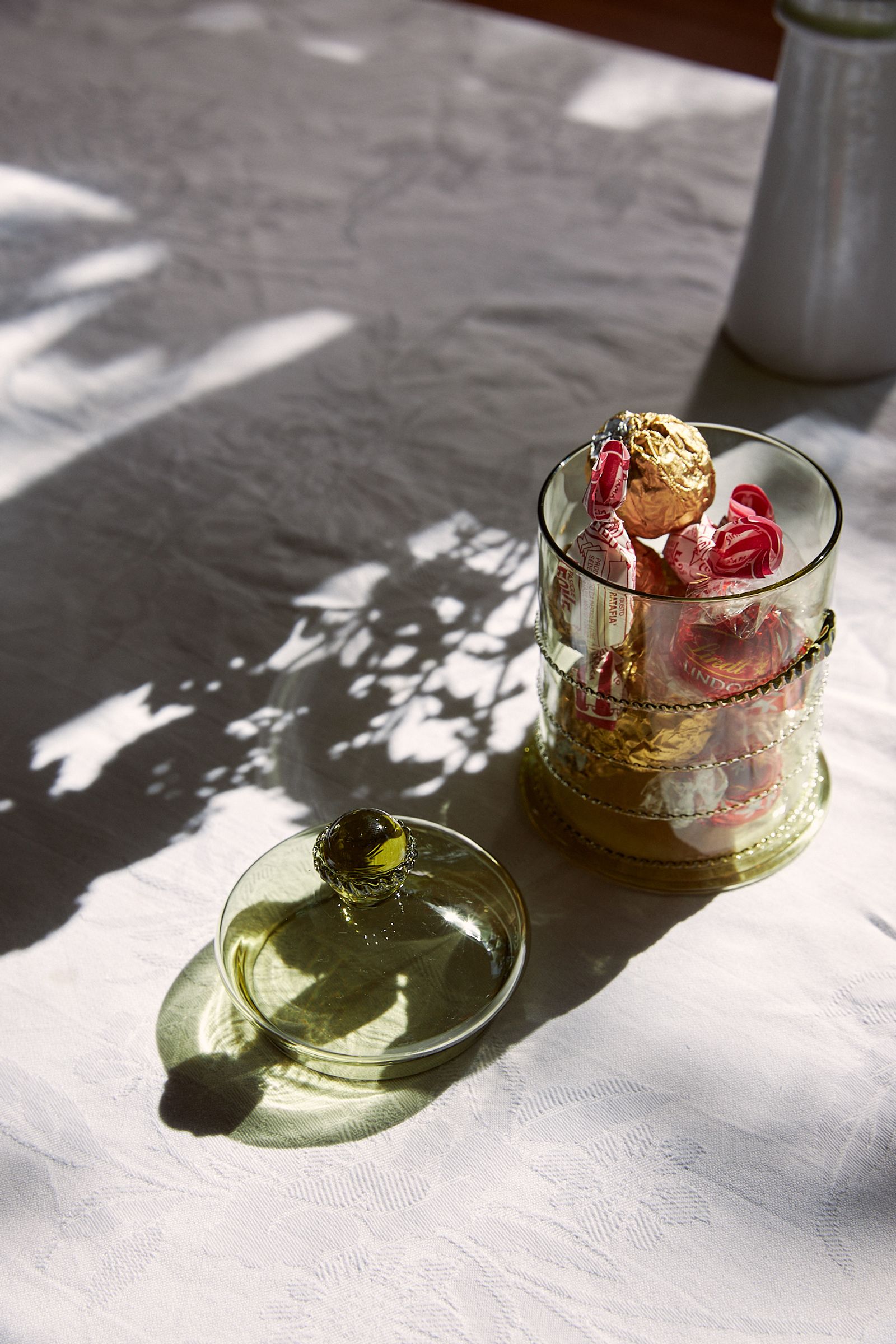 green glass jar sits with lid off on a table with white linen
