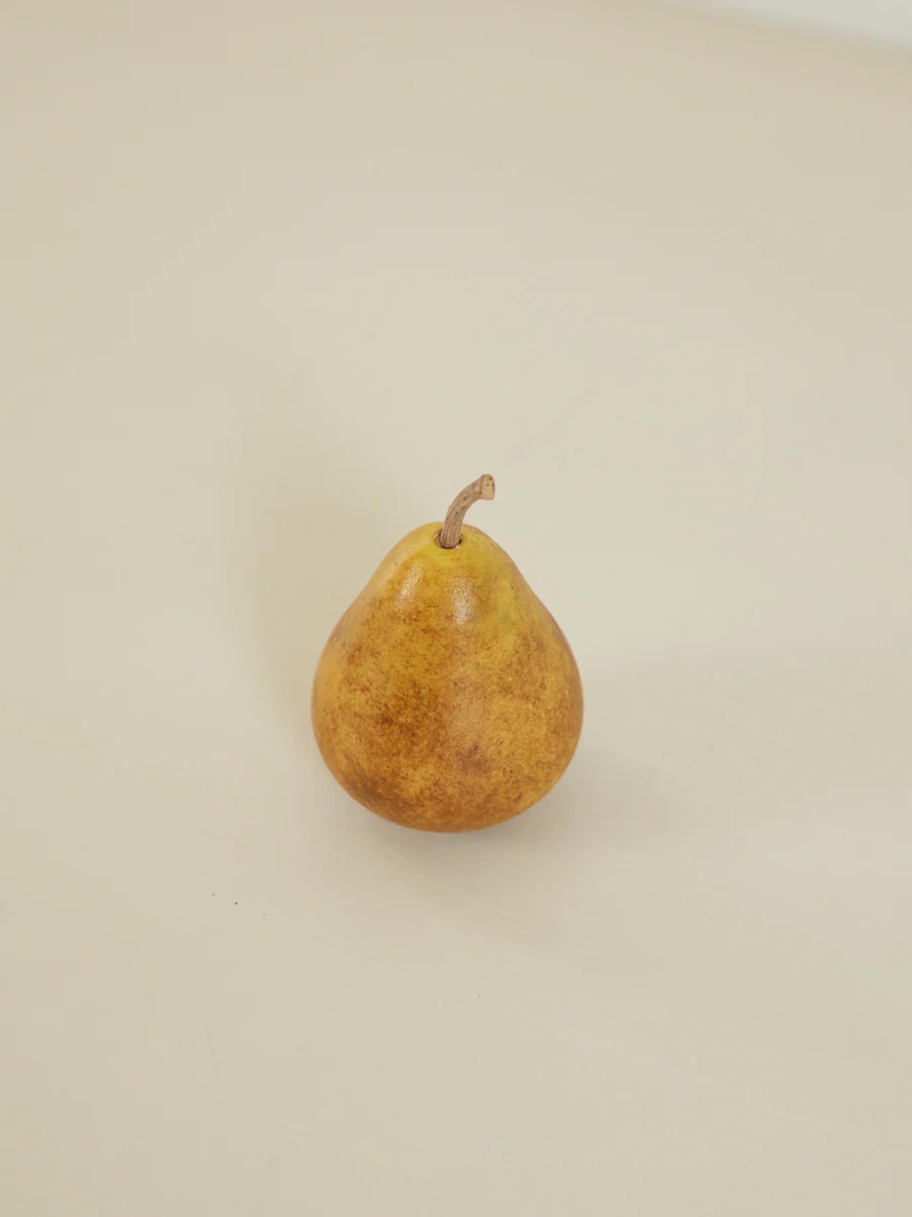 Single brown pear with short stem on light Carrara marble surface. Minimalist composition highlights pear's shape.