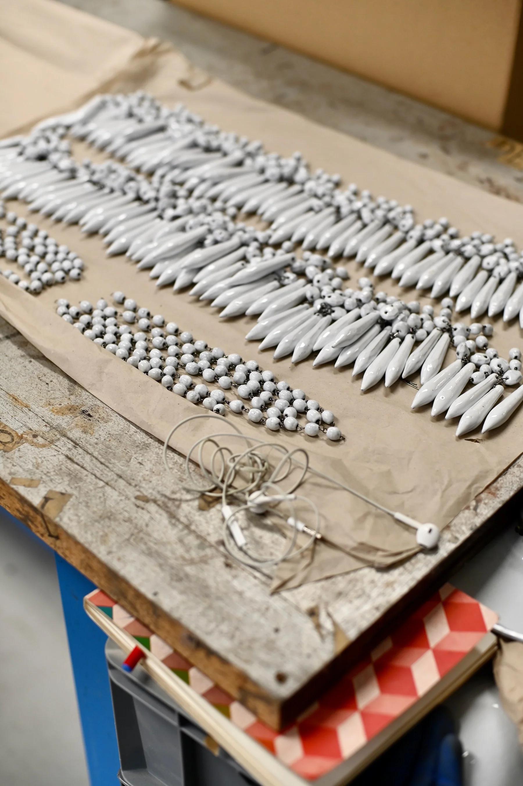 White ceramic pieces including elongated shapes and spherical beads with black patterns on brown paper. Tangled white earphones nearby.