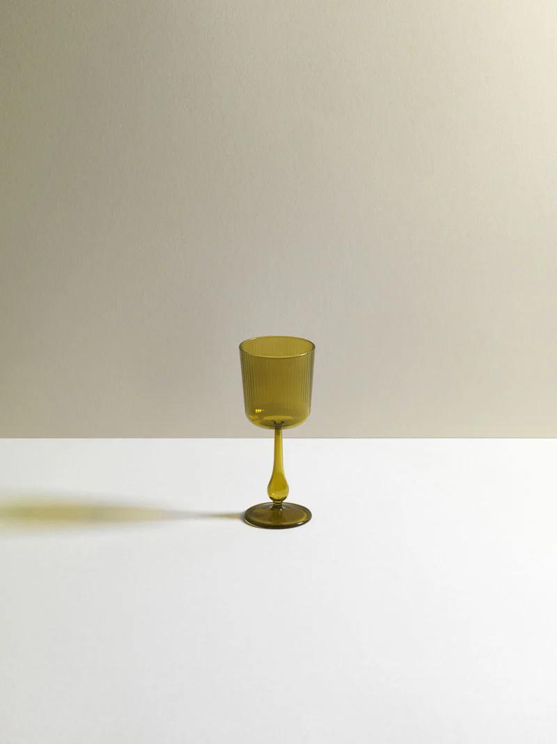 Single olive green R+D.LAB wine glass on white-beige gradient background. Sleek design casts subtle shadow, highlighting studio's research-driven approach.