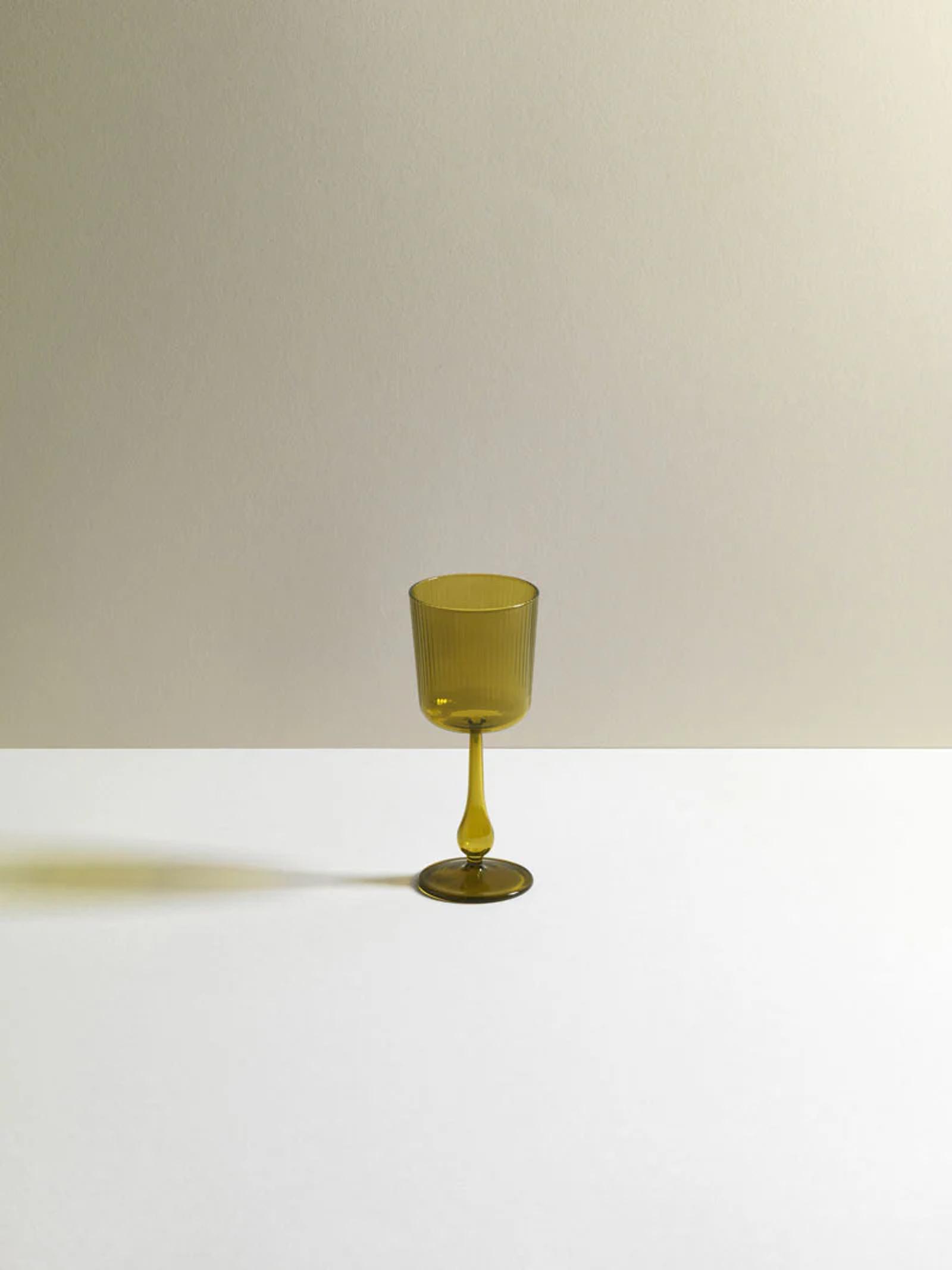 Single olive green R+D.LAB wine glass on white-beige gradient background. Sleek design casts subtle shadow, highlighting studio's research-driven approach.