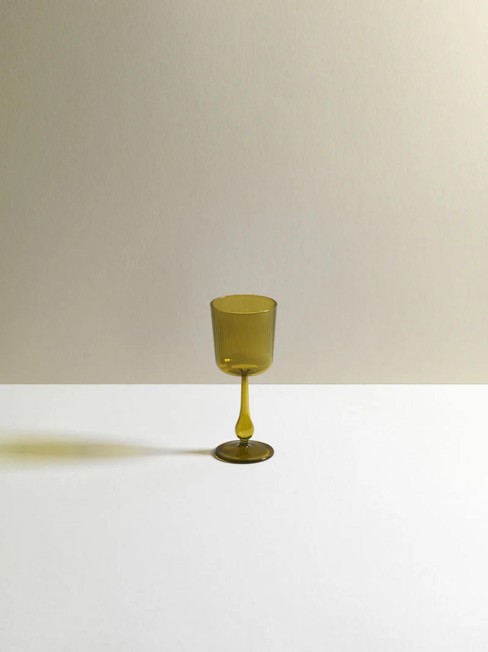Single olive green R+D.LAB wine glass on white-beige gradient background. Sleek design casts subtle shadow, highlighting studio's research-driven approach.