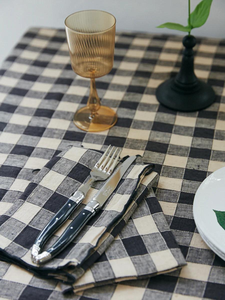 Black and white checkered tablecloth, folded napkin with utensils. Amber glass, black candlestick with green sprig.