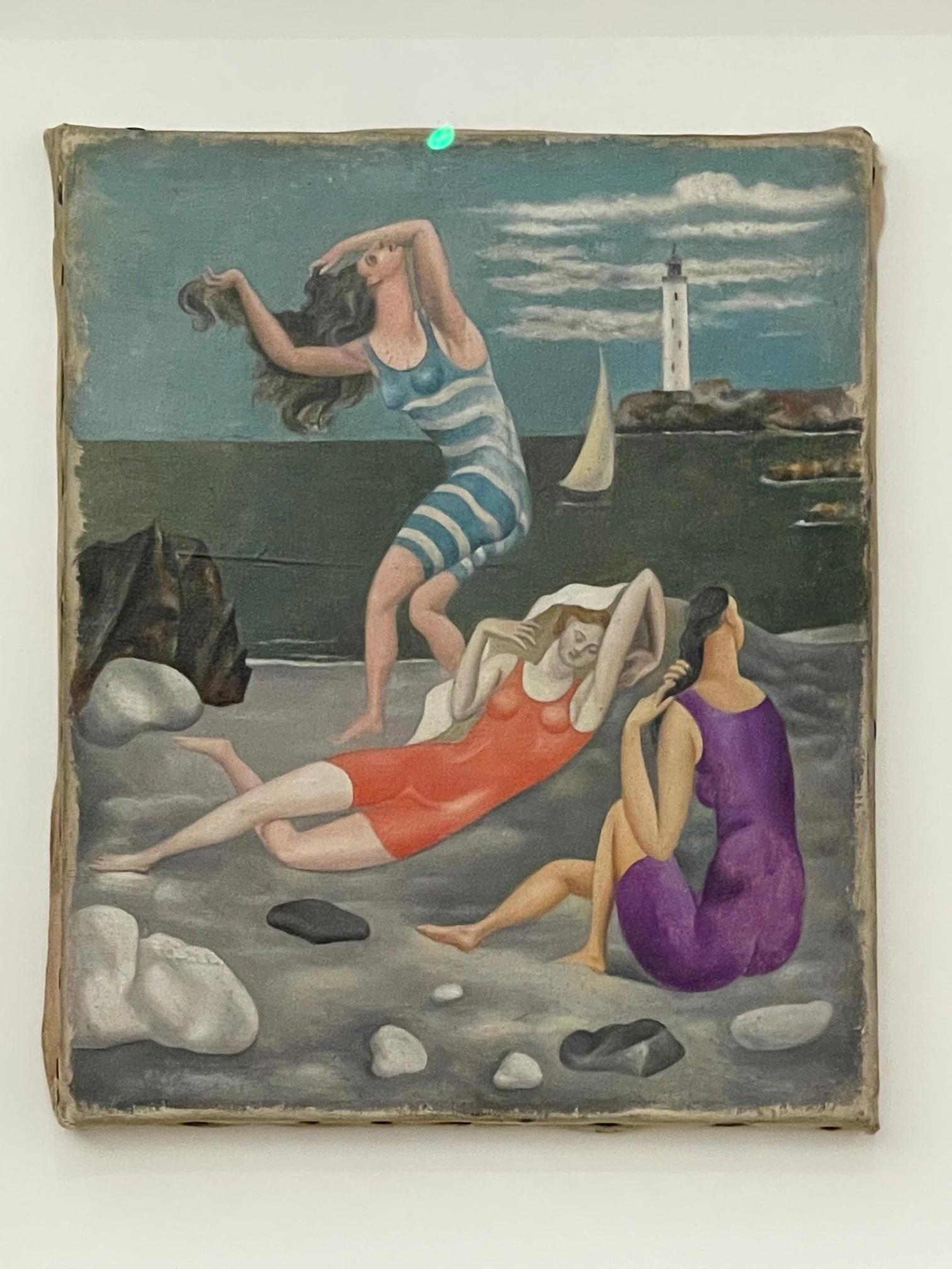 Painting of three women in swimsuits on rocky beach. Lighthouse and sailboat in background. Partly cloudy sky, calm sea.