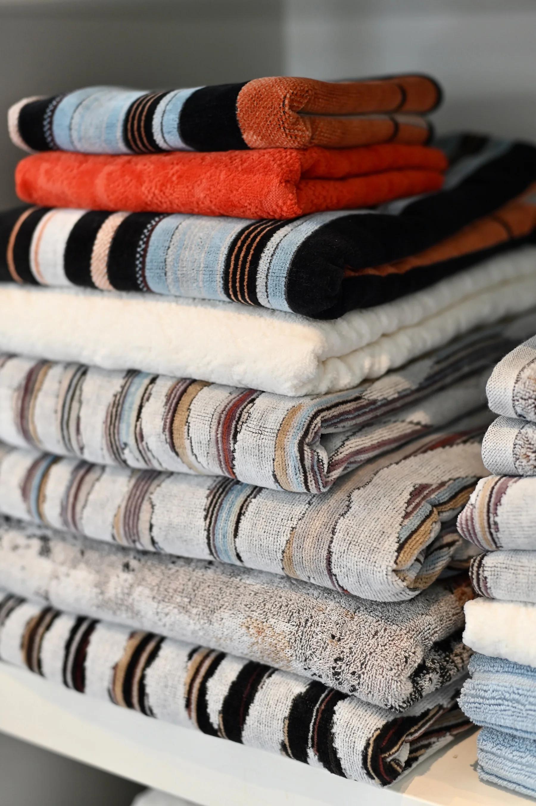 Stacked towels in various colours and patterns on shelf. Soft, fluffy fabric inspired by Australian landscapes.