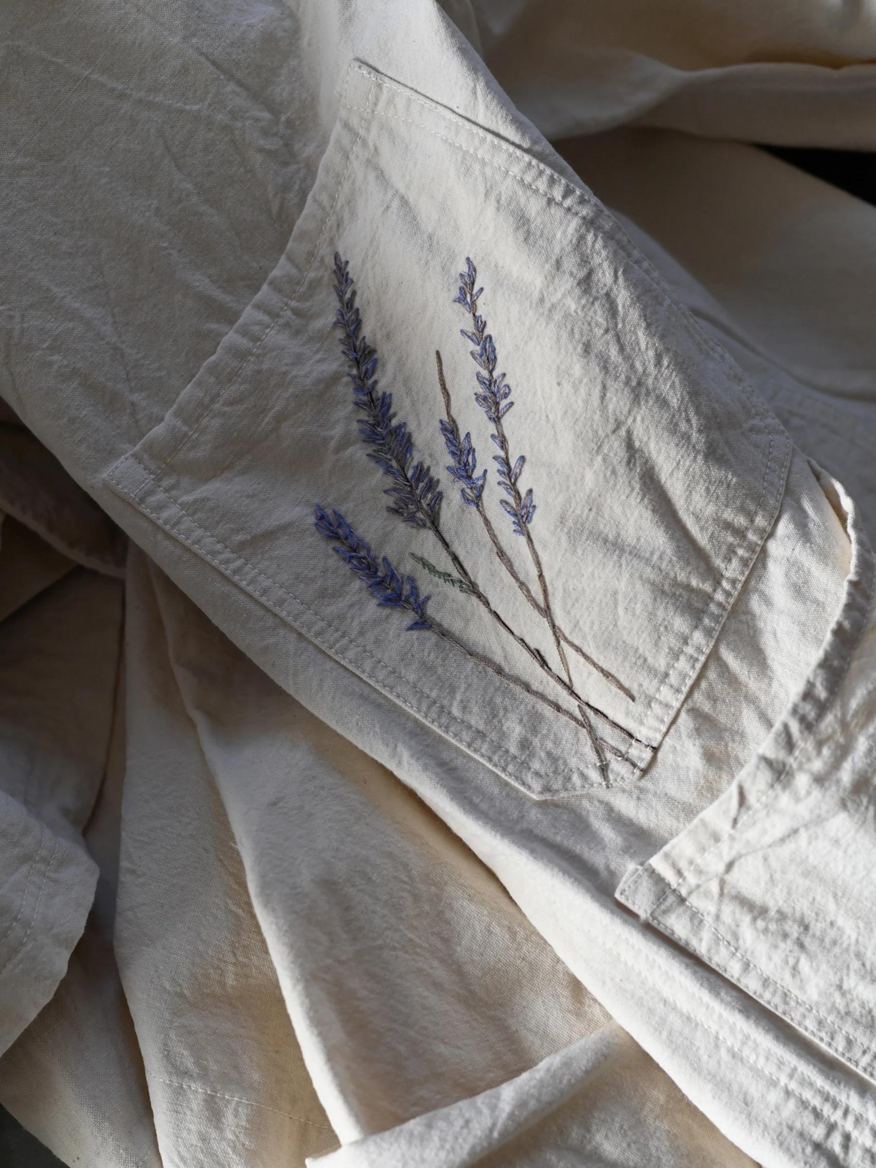Beige Oliver Church fabric with embroidered lavender sprigs on pocket. Wrinkled texture shows Singular Garments' practical design.