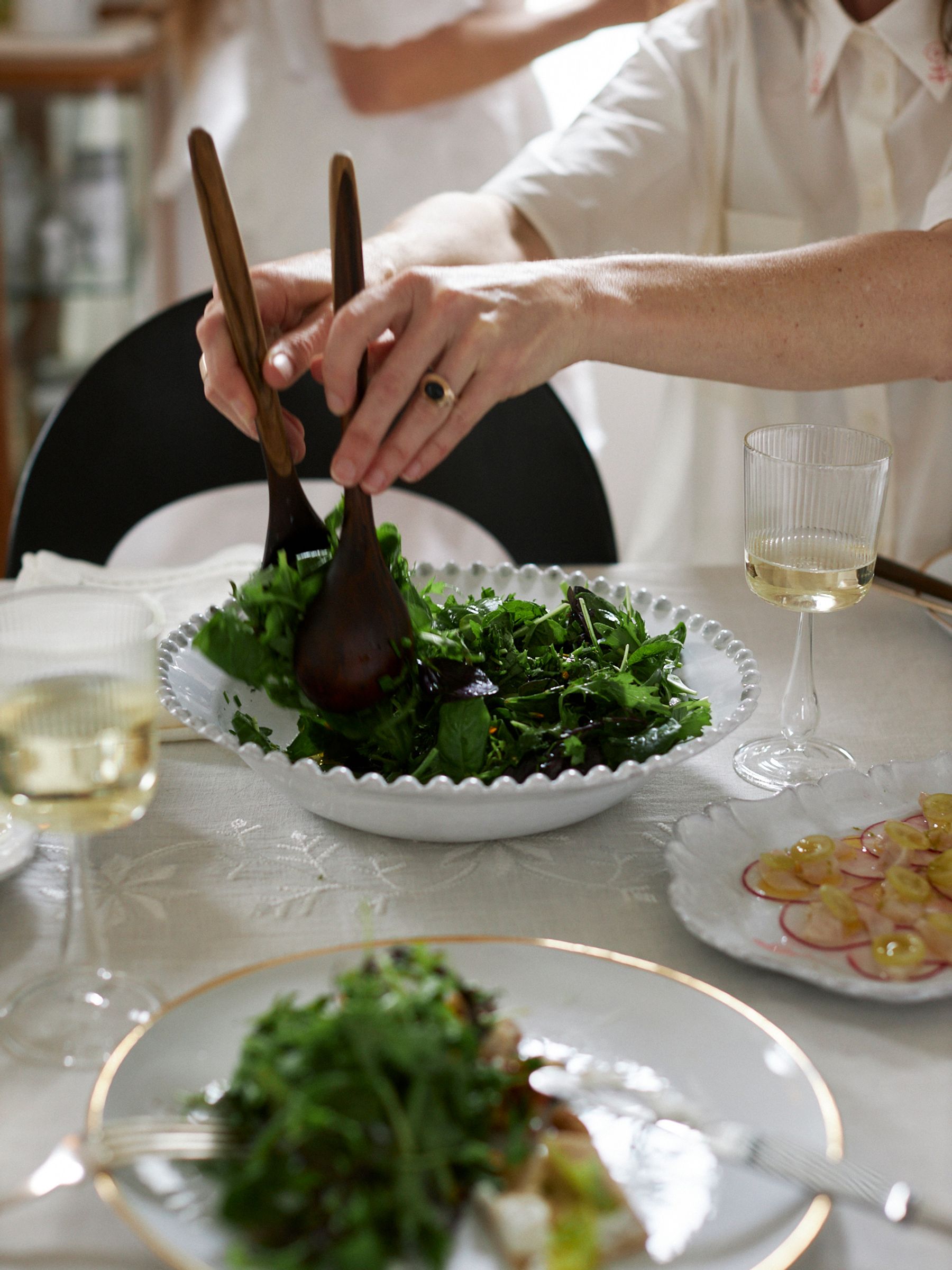 woman serves salad from tastier de village bowl on table with wine glasses