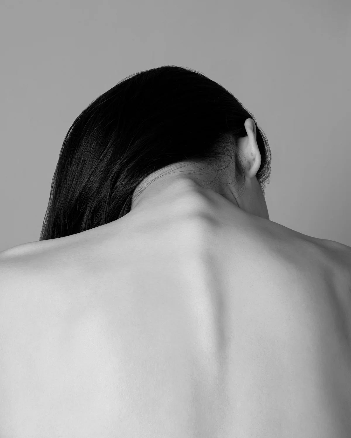 Black and white photo of person's back and head. Long, dark hair to one side, exposing spine and neck.