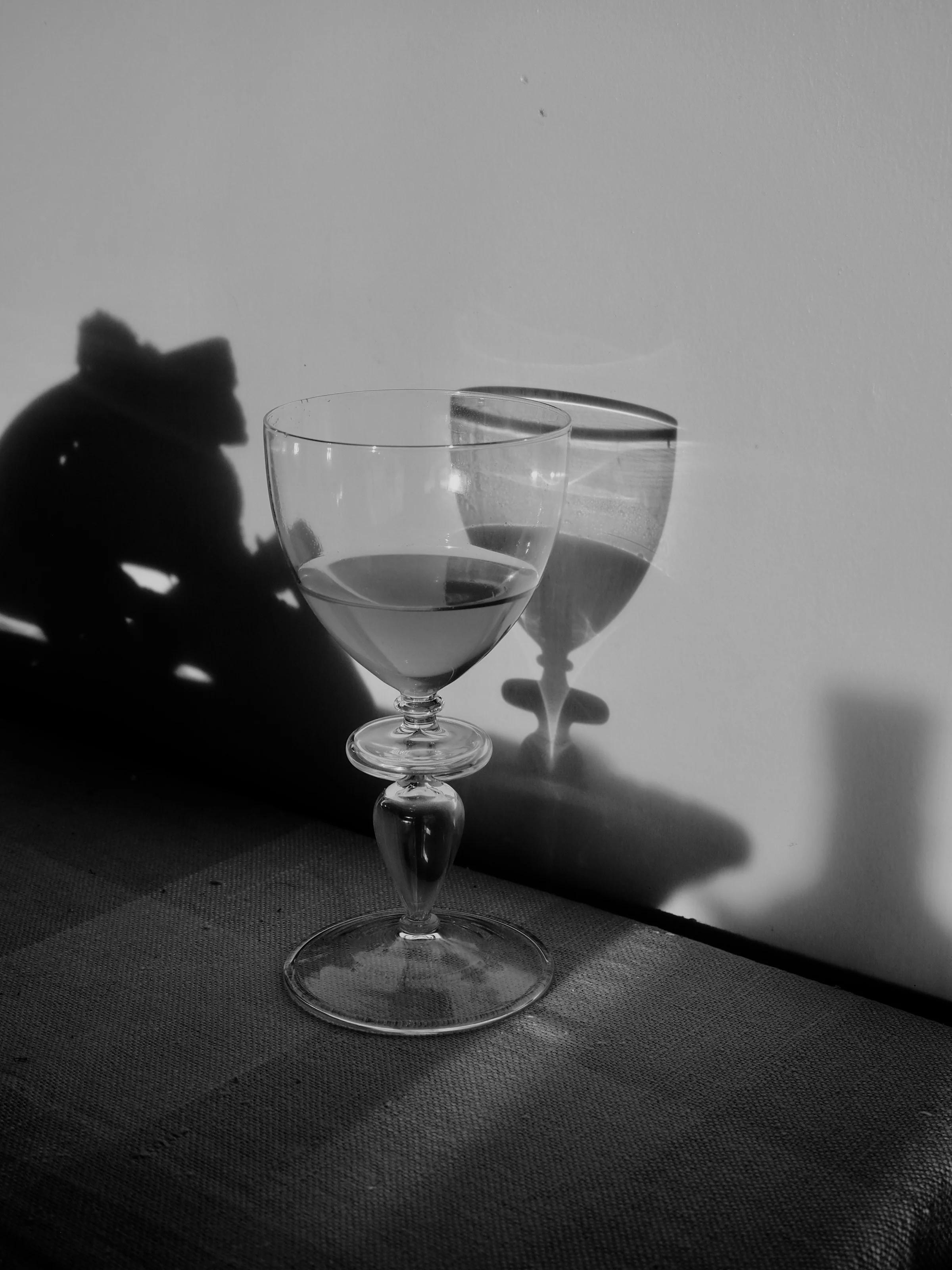 Glass of organic wine casting shadow on textured surface. Partial view shows curvature and details in black and white, emphasising light and shadow interplay.