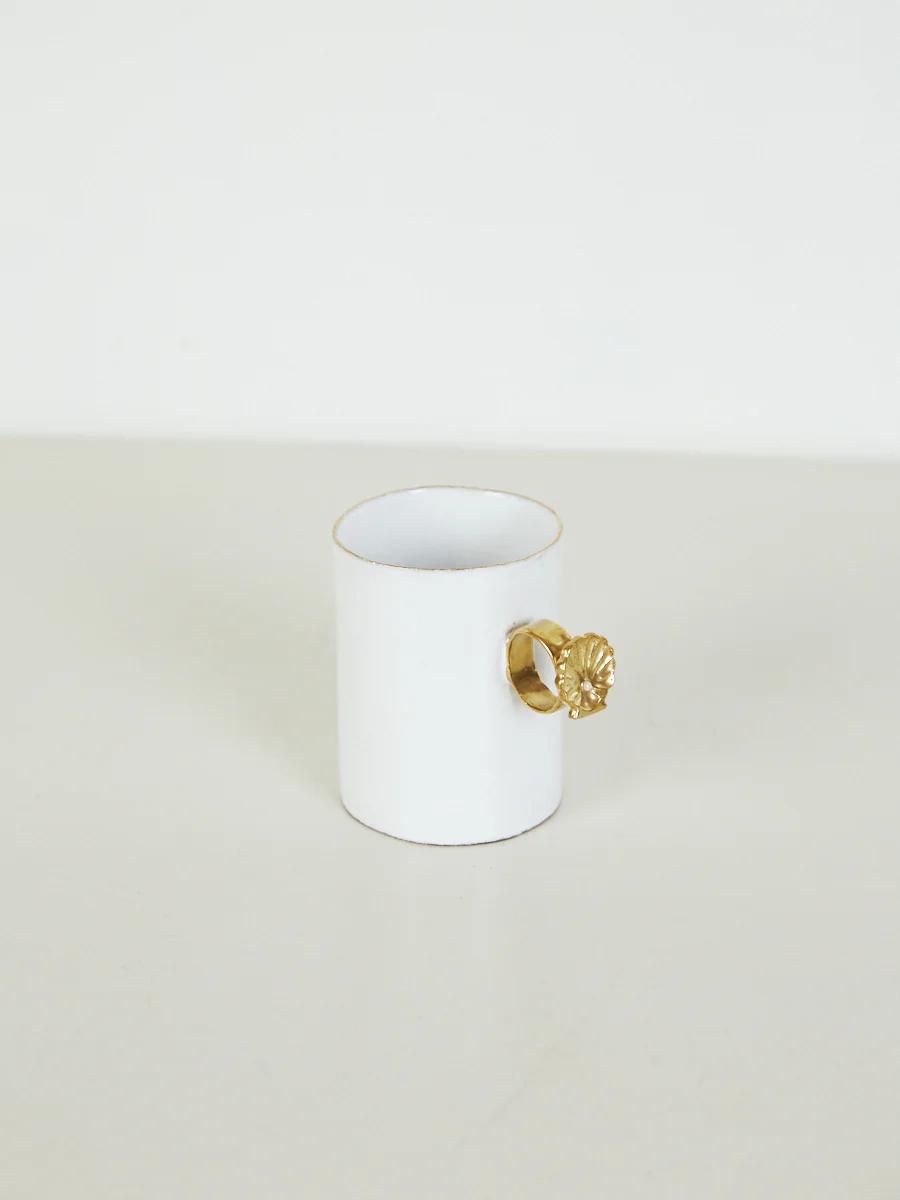 Small white ceramic cup with gold rim and lion head handle on light surface.