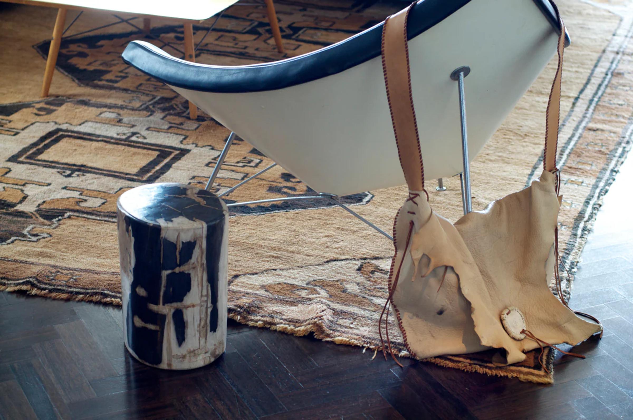 Modern living room with geometric rug and unique black and white stool. Stylish chair with leather backrest draped with light-coloured hide on dark wooden floor.