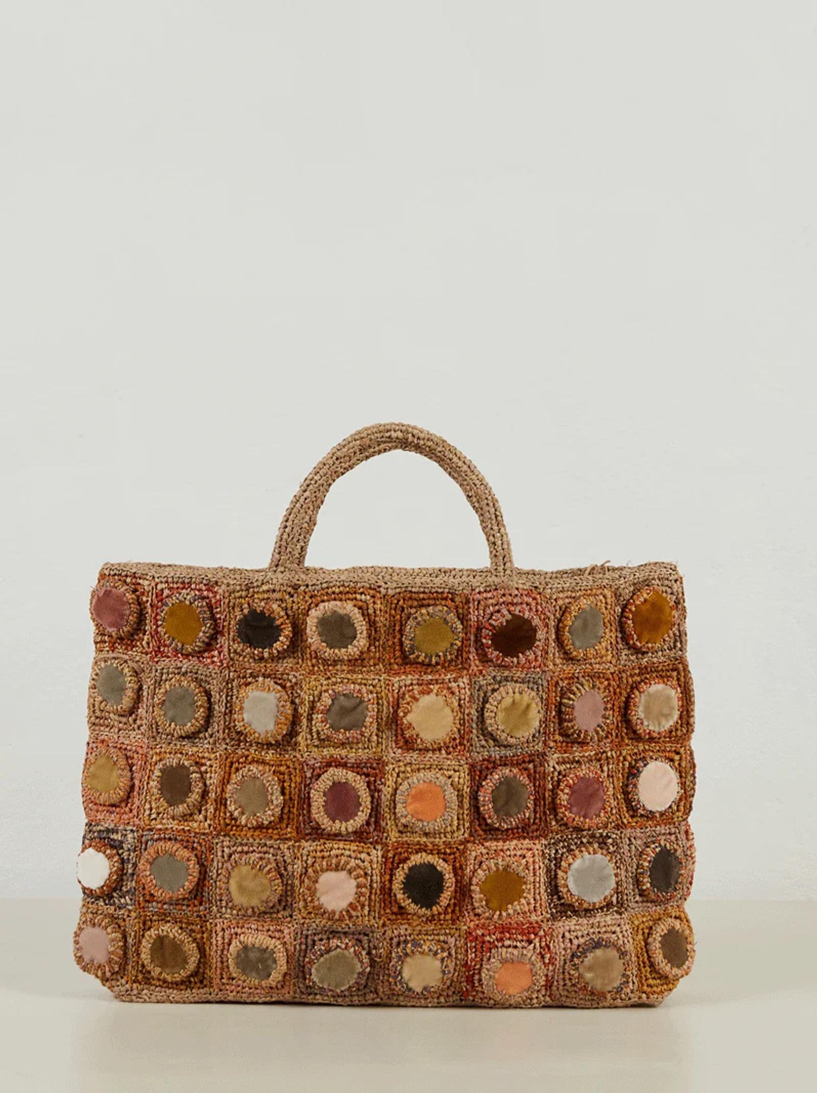 Woven handbag with short handles, featuring circular patches in earthy tones. Textured, rustic appearance similar to Sophie Digard's creations. Displayed on white background.