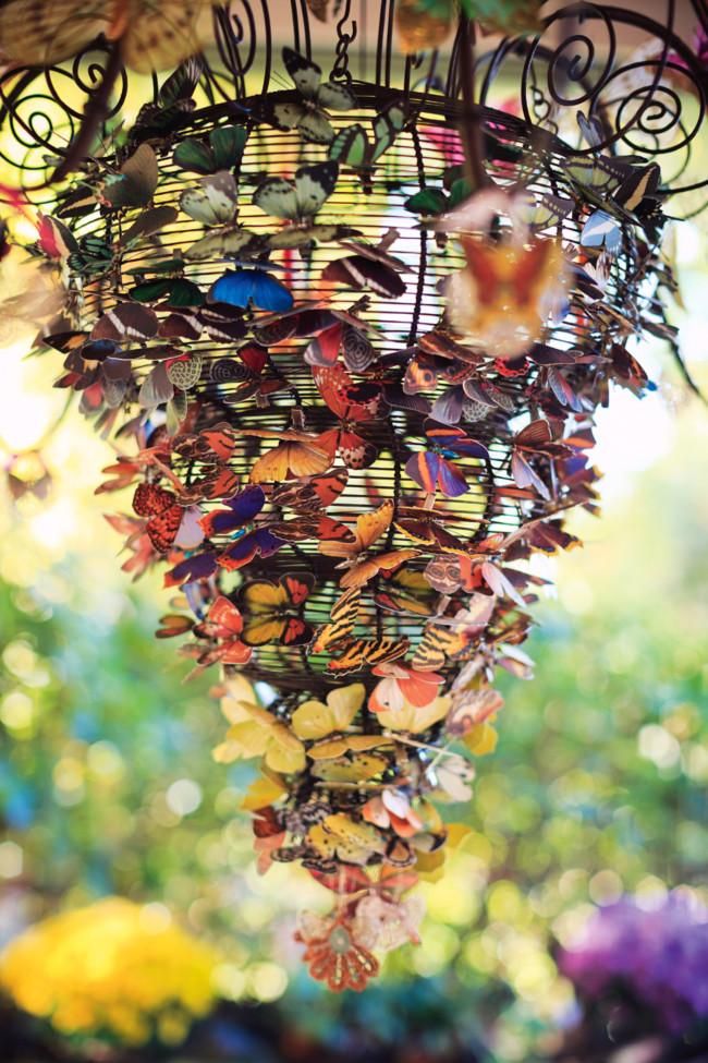 Hanging spiral chandelier made of colourful artificial butterflies. Blurred background of sunlight and greenery.