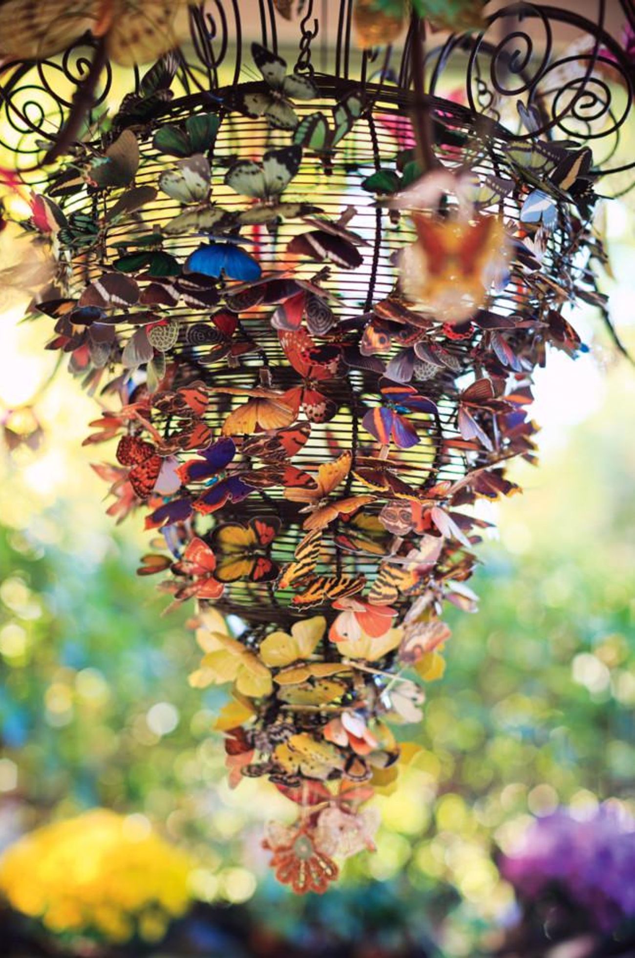 Hanging spiral chandelier made of colourful artificial butterflies. Blurred background of sunlight and greenery.