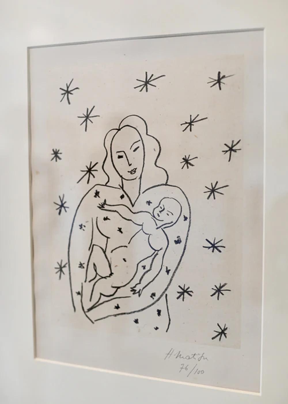 A black and white drawing depicts a woman holding a baby surrounded by stars. The minimalist style uses simple lines to form the figures. This framed artwork is signed "H. Matisse 76/100,".