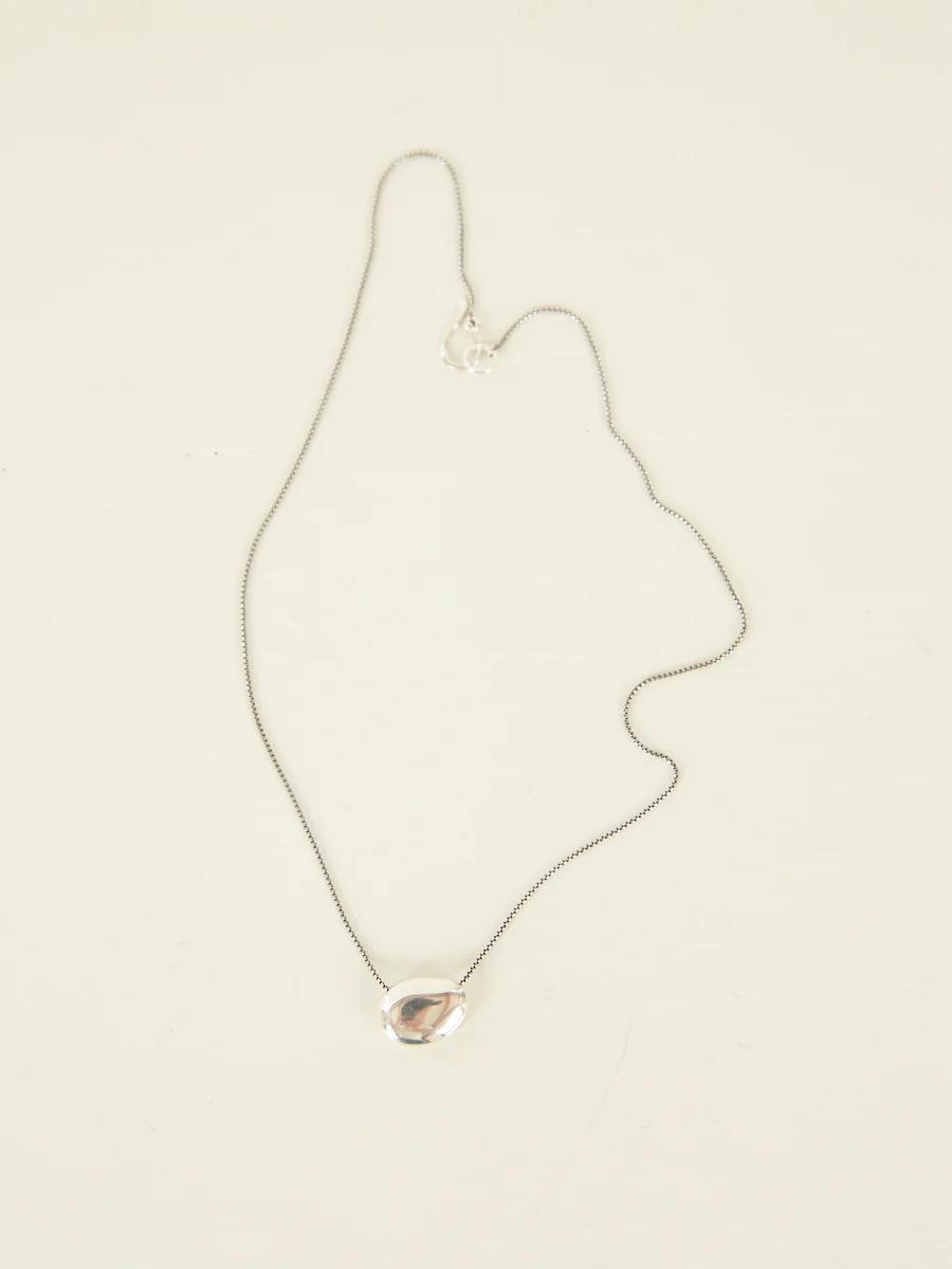 Delicate silver chain necklace with teardrop-shaped crystal pendant on white surface.