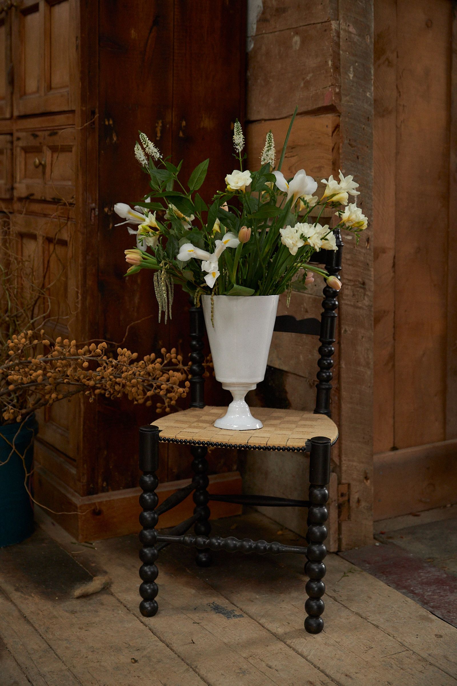 vase of flowers sits on a woven chair in the barn