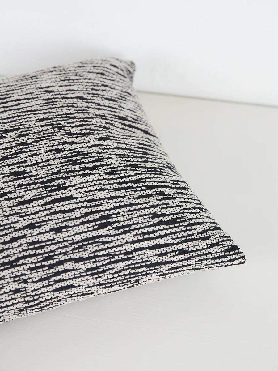 Close-up of black and white chevron pillow. Angled on light-coloured surface.