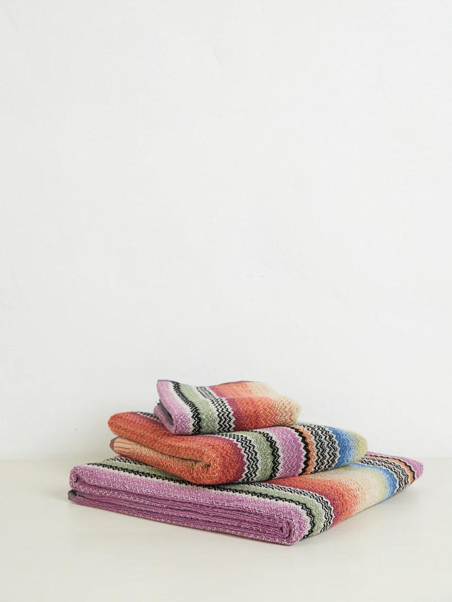 A folded stack of Missoni towels with horizontal stripes in purple, orange, green, and pink, on a light surface.