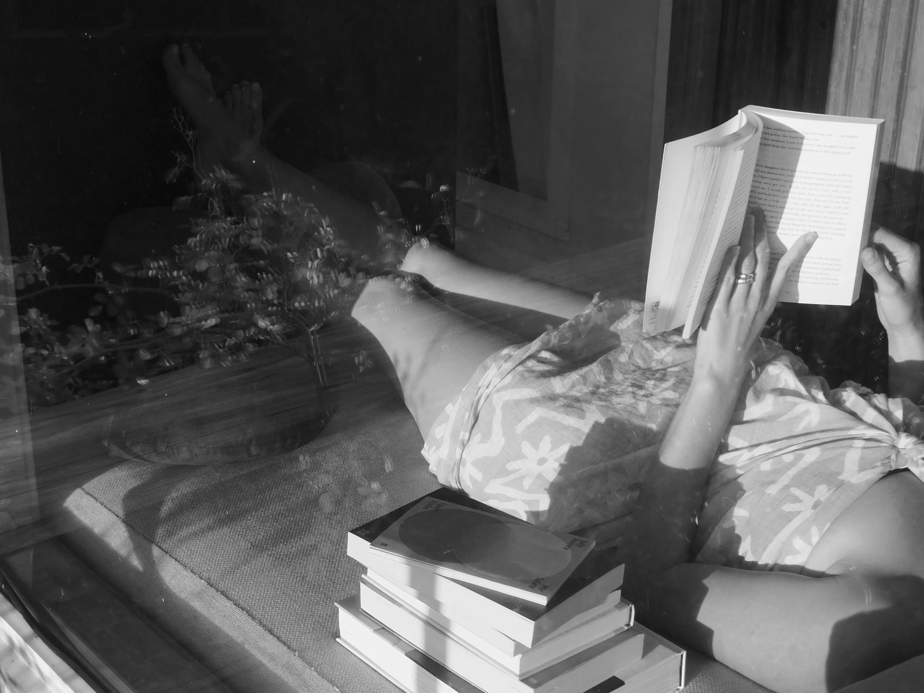 Black and white photo of someone reading, legs visible through a window. A stack of books nearby suggests a restful Easter break scene.