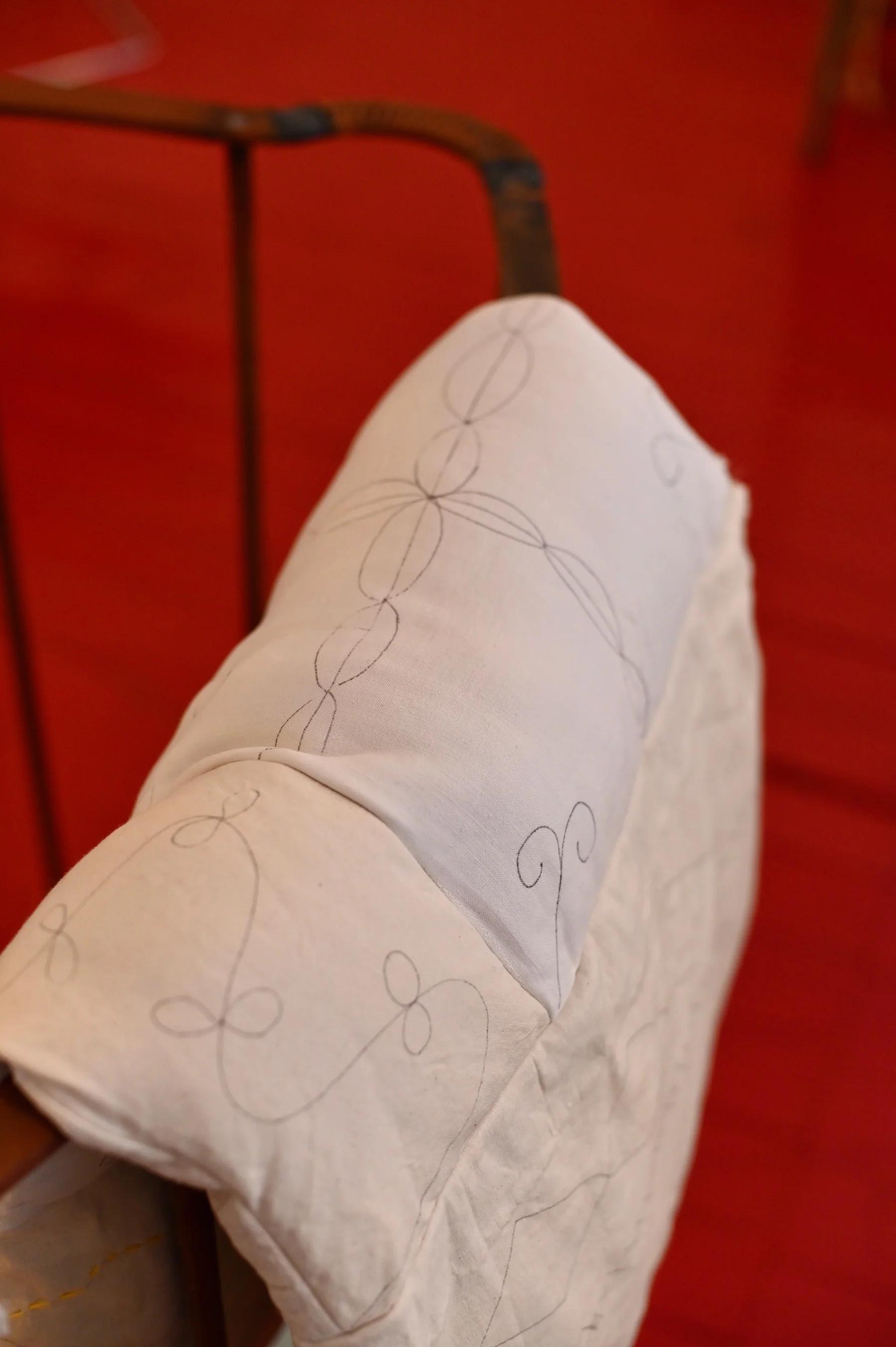 Close-up of light-coloured quilt with delicate embroidery on wooden chair. Vivid red background.