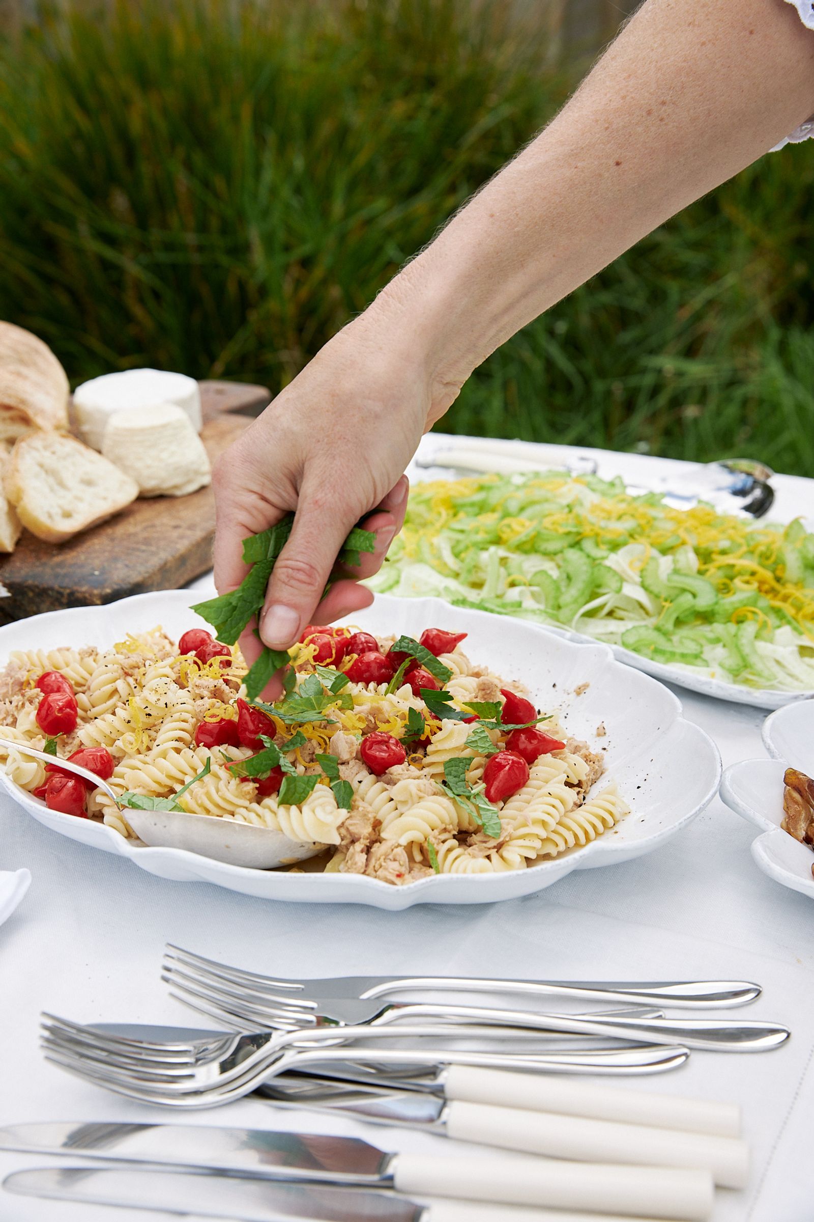 hand sprinkles fresh herbs over a platter of fusilli salad