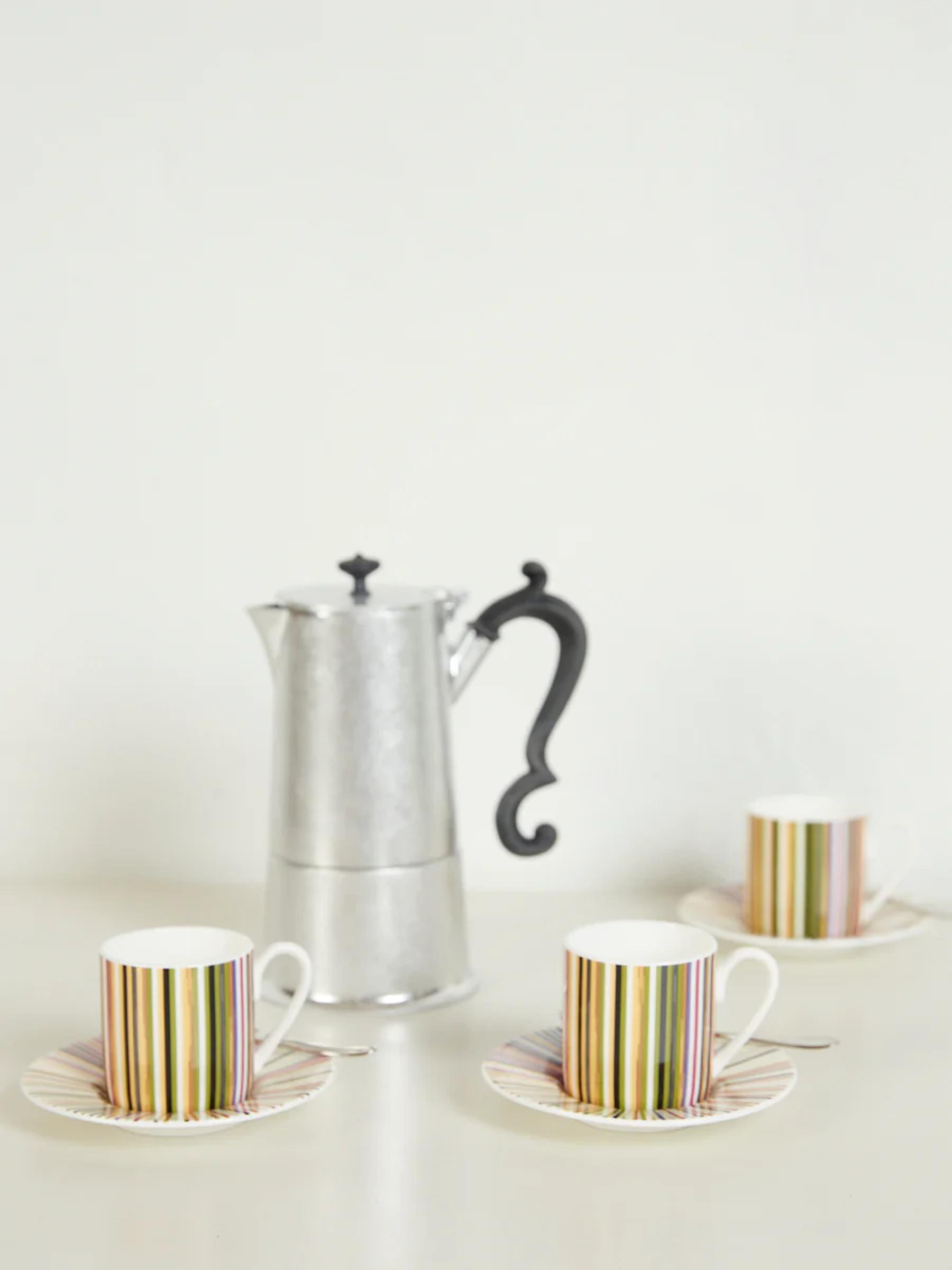 Silver espresso maker with three white mugs with colourful vertical stripes. White surface and background.