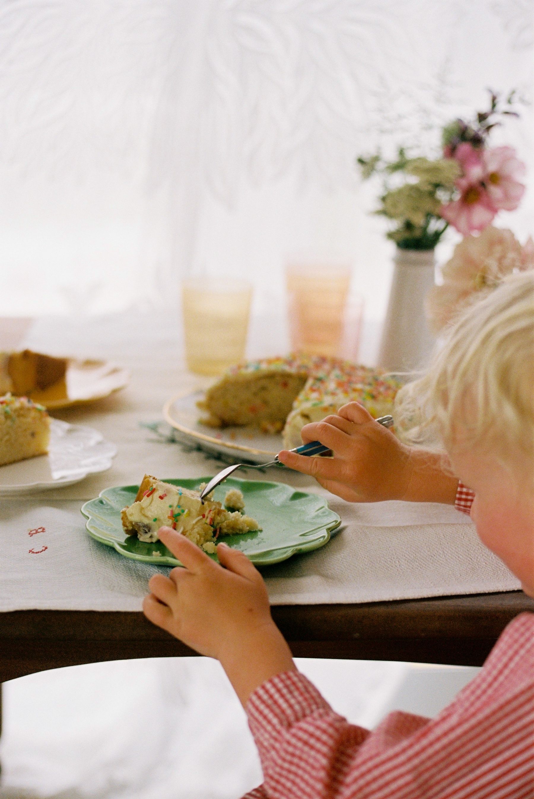 small boy eats his cake at the table covered in flowers and coloured glasses