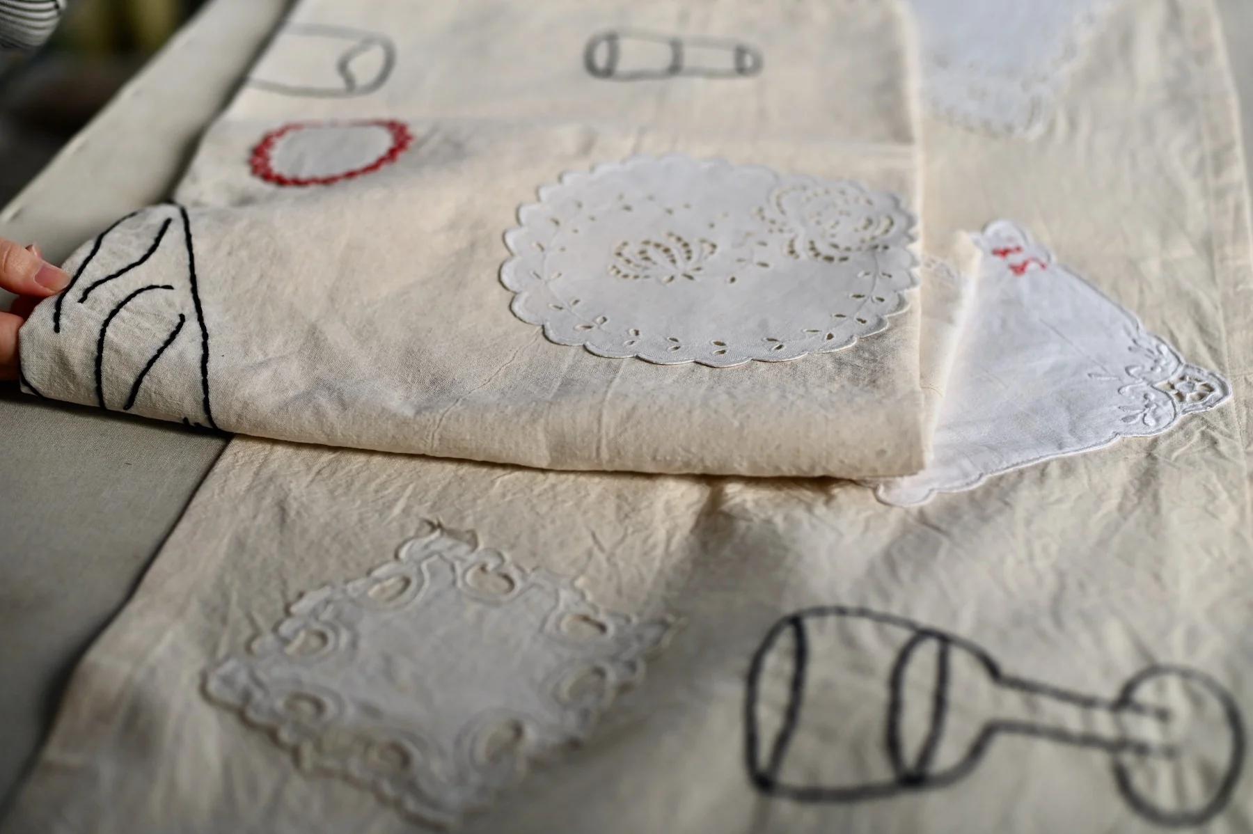 Person holds folded embroidered fabric with various stitched designs. Flat surface in background.