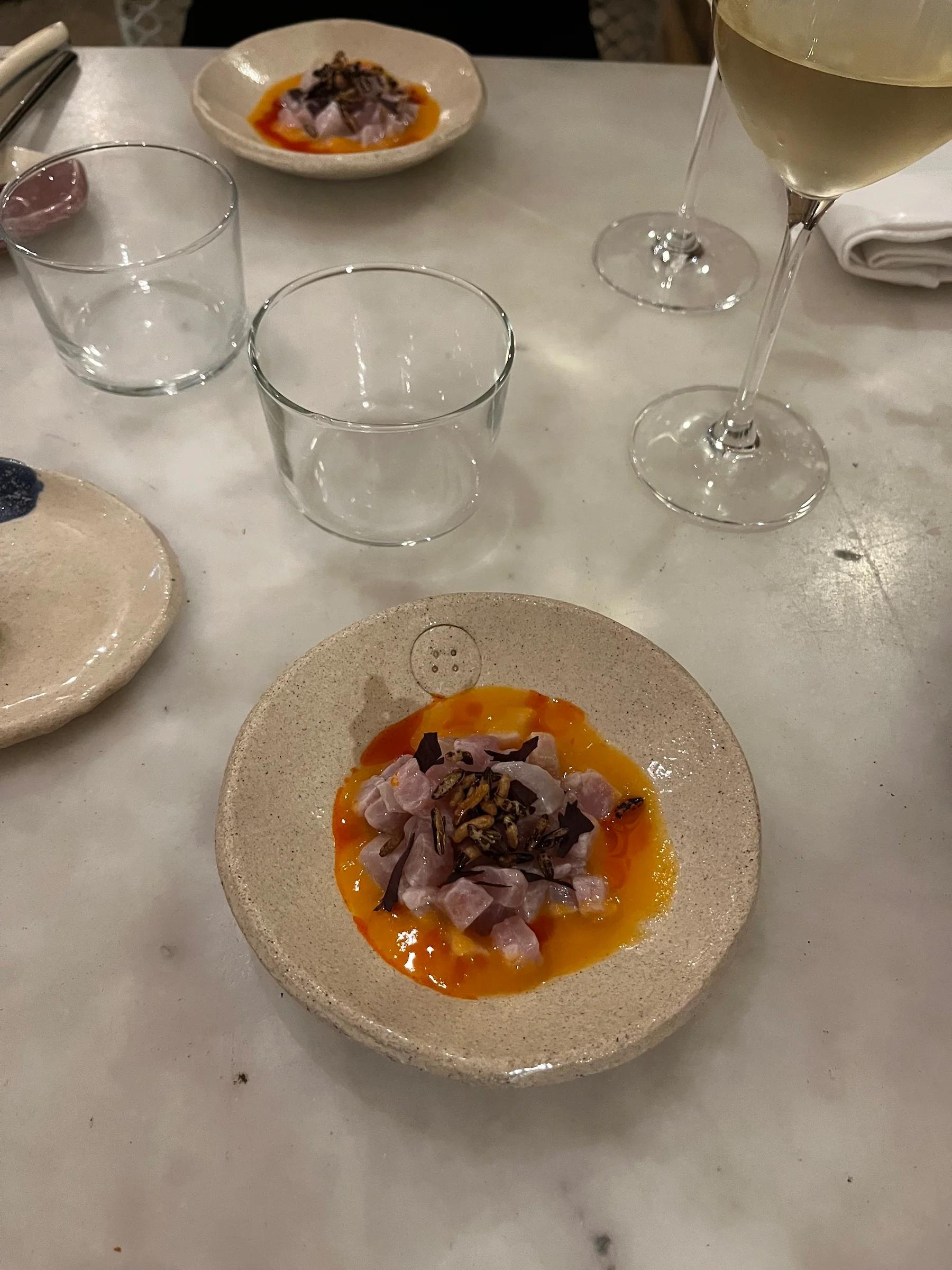 Fine dining table with diced fish in red-orange sauce. Empty glasses, white wine, and napkin complete the elegant Marseille bistro setting.