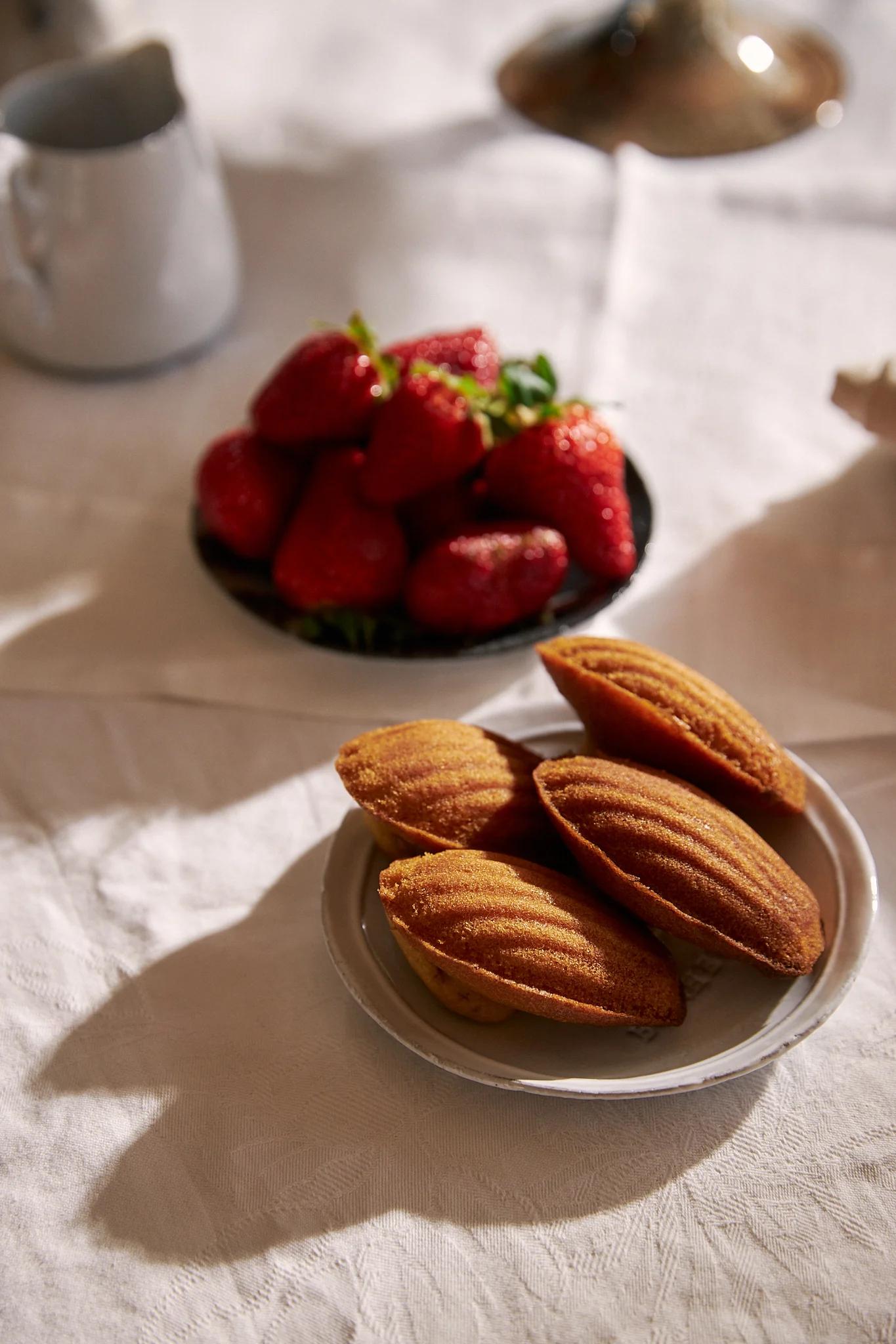 French madeleines nestled on a white plate in front of a bowl of strawberries