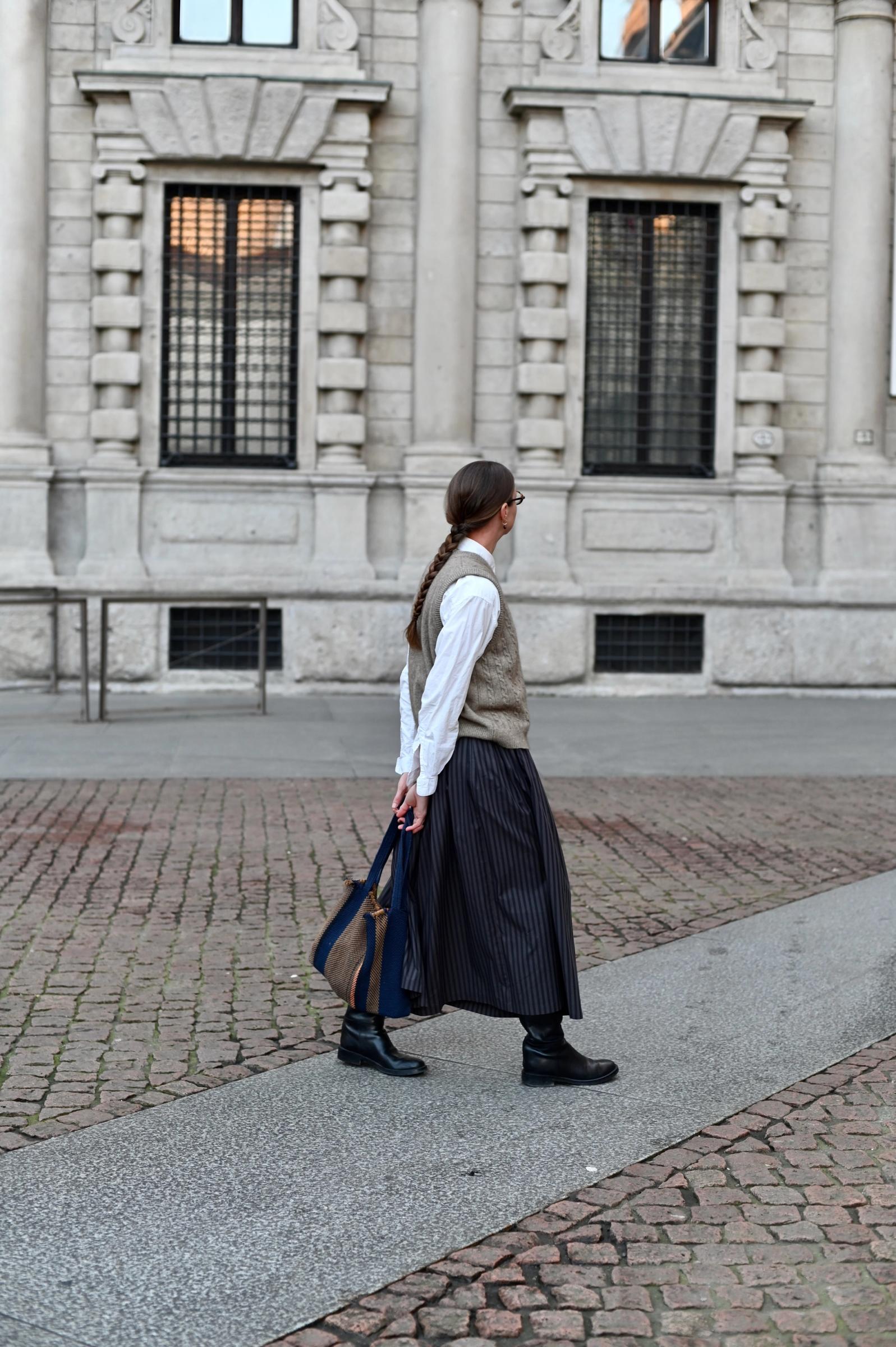 women walking around stone buildings in wool vest and striped skirt
