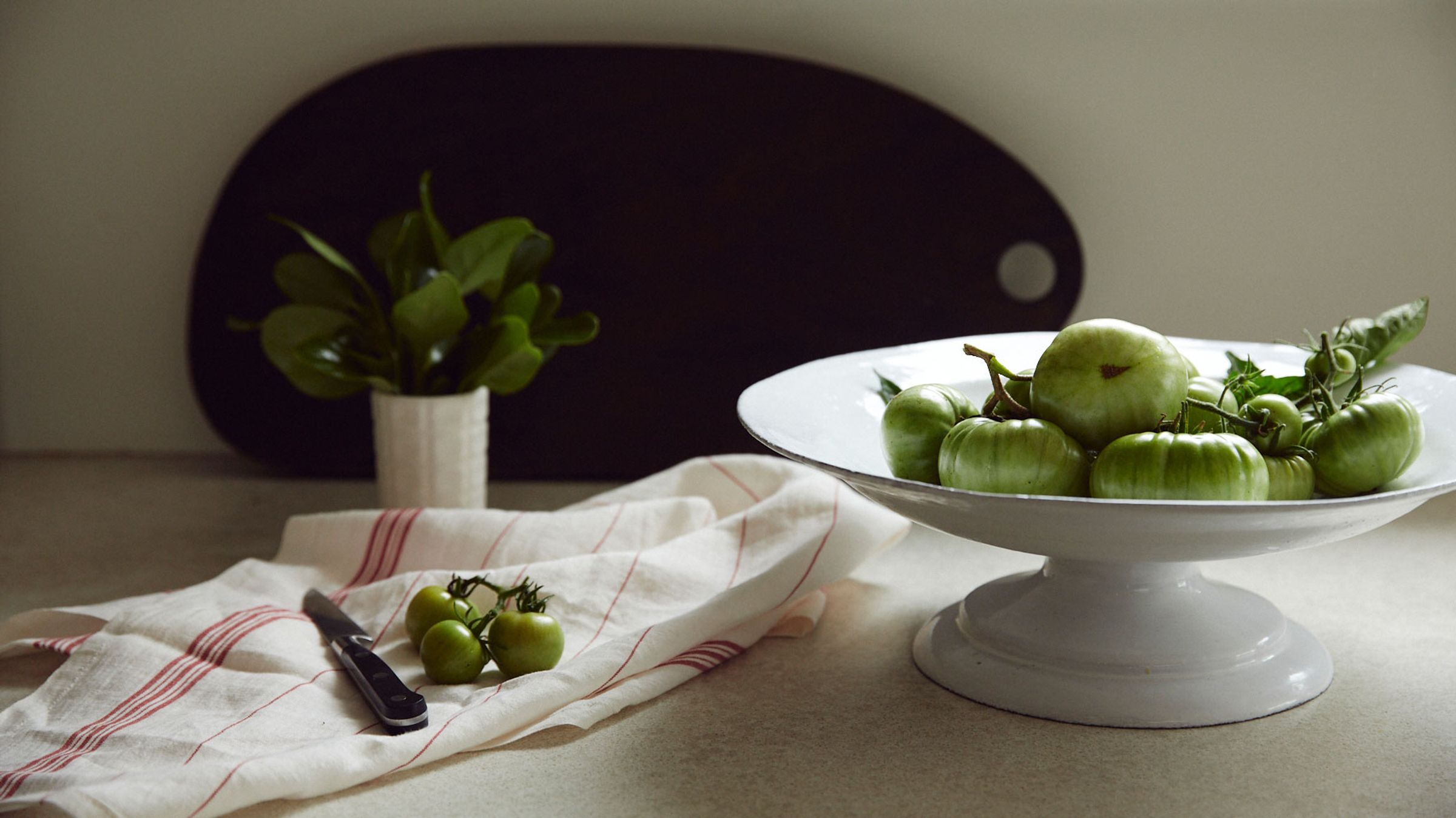 Ceramic fruit stand with green tomatoes on kitchen bench