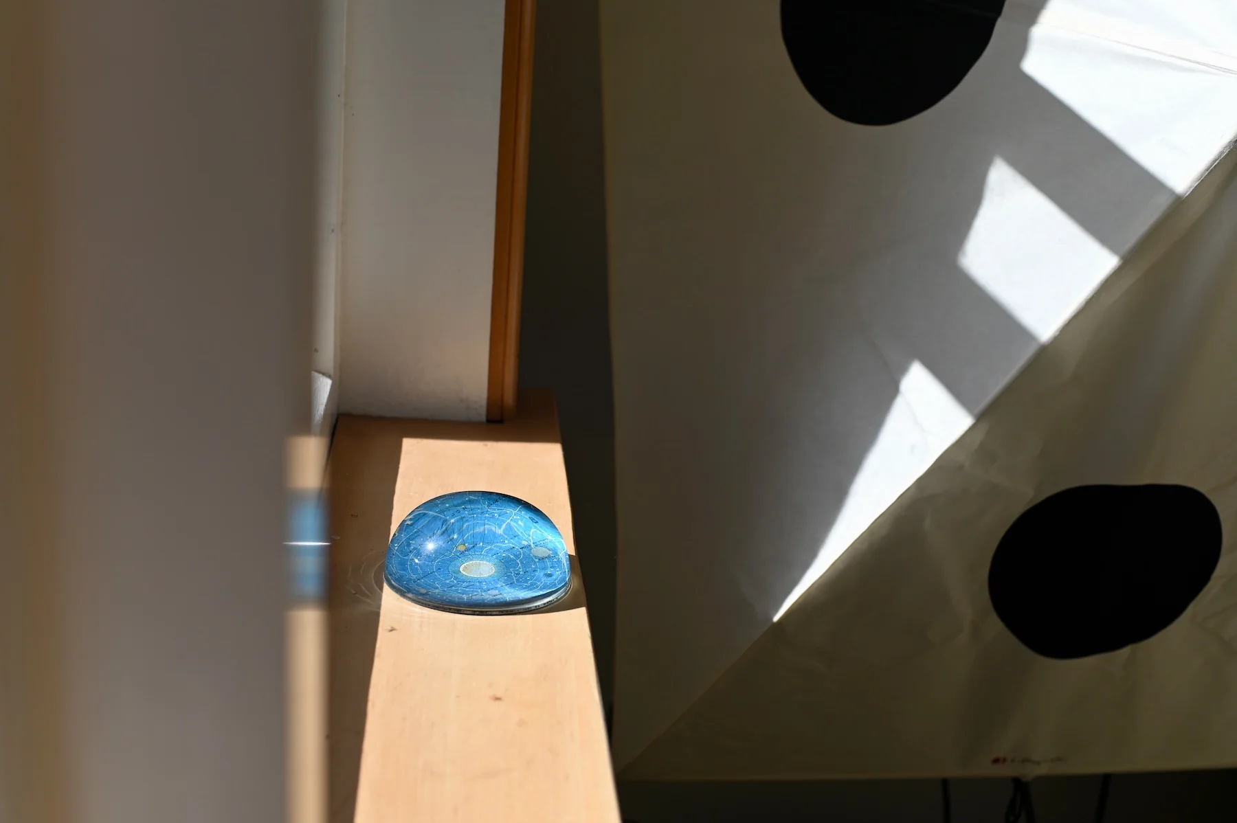 Blue decorative object on wooden ledge. Geometric window shade casts shadows on wall.