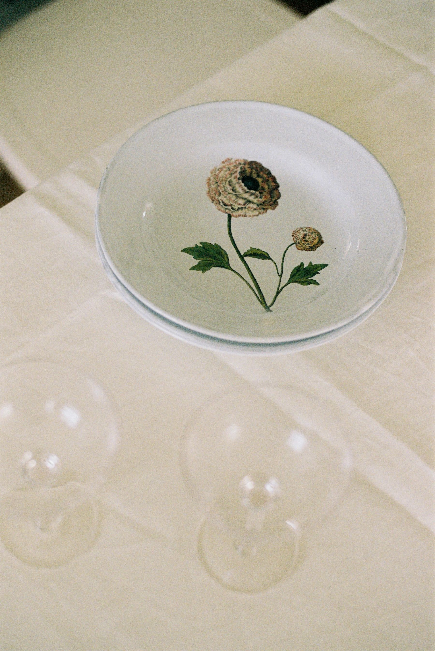 a hand painted plate featuring a frilly flower sits besides two champagne saucers