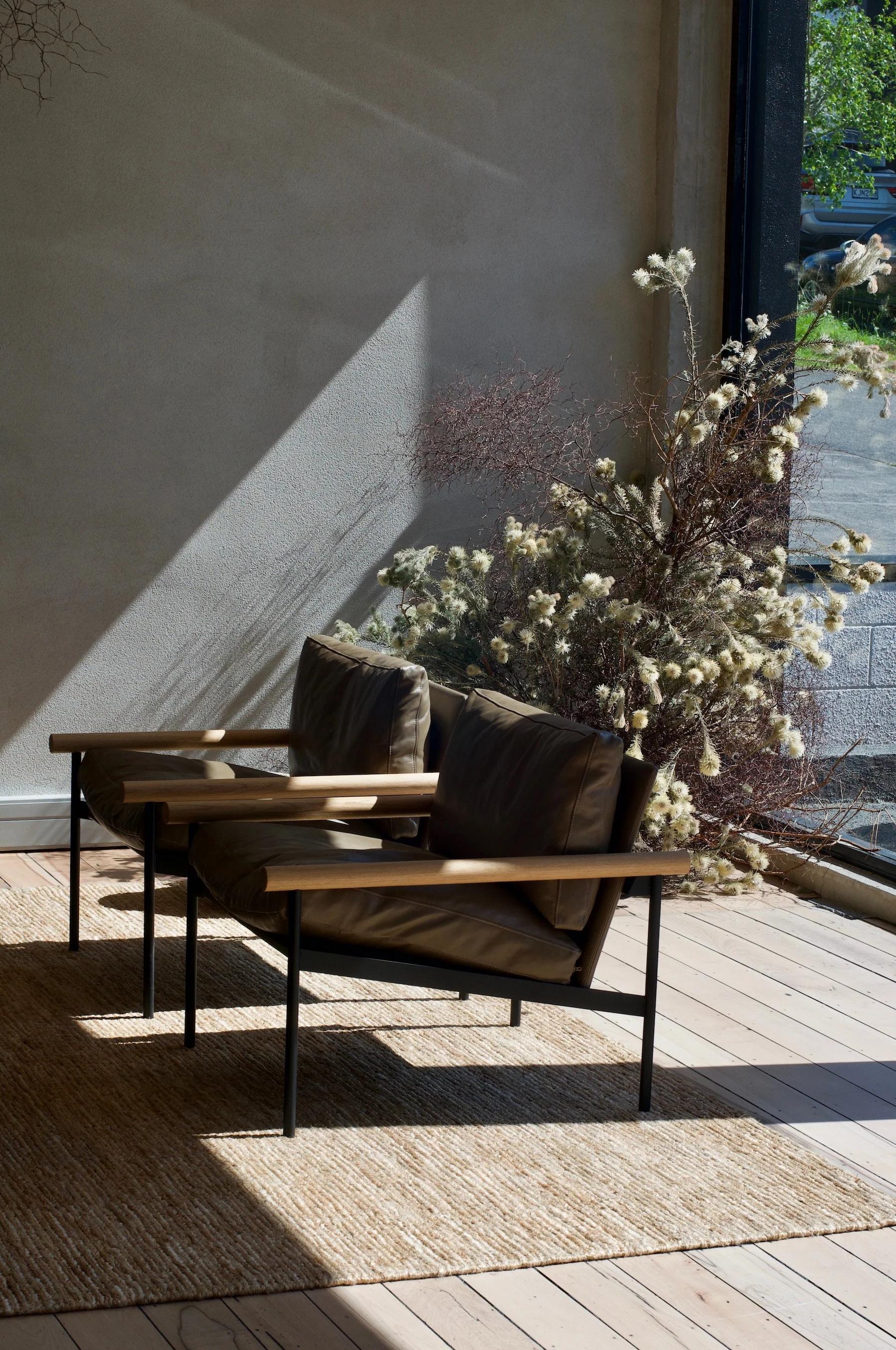 Modern sitting area with leather chairs on rug. Sunlit room with dried plants against neutral wall.