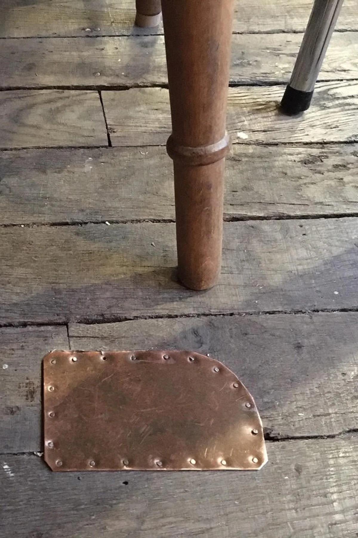 Wooden table leg and metal chair leg on rustic floor. Metal plate with rivets partially embedded in floorboards.