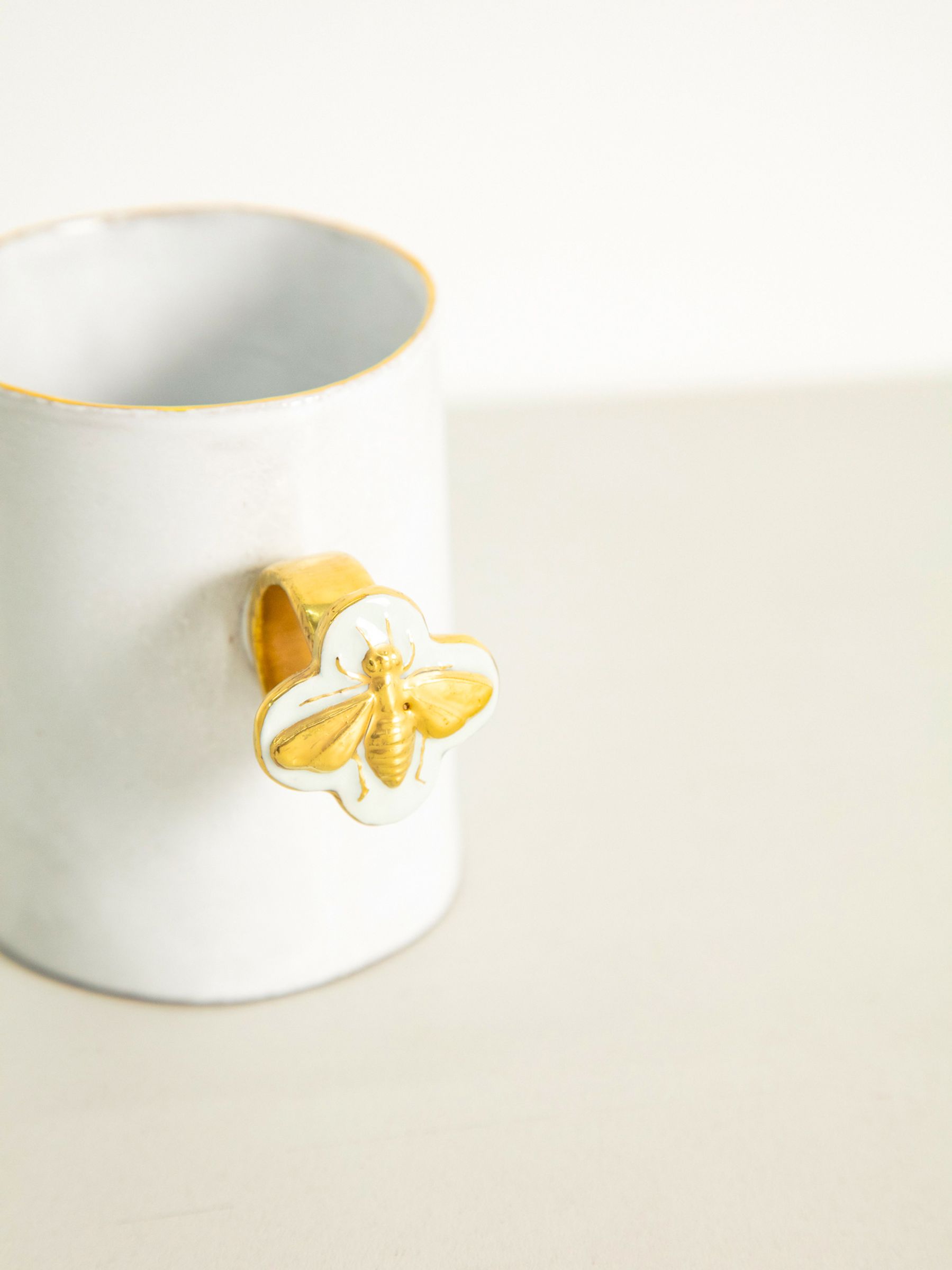 White mug with bee shaped handle. Light-coloured surface, white background.