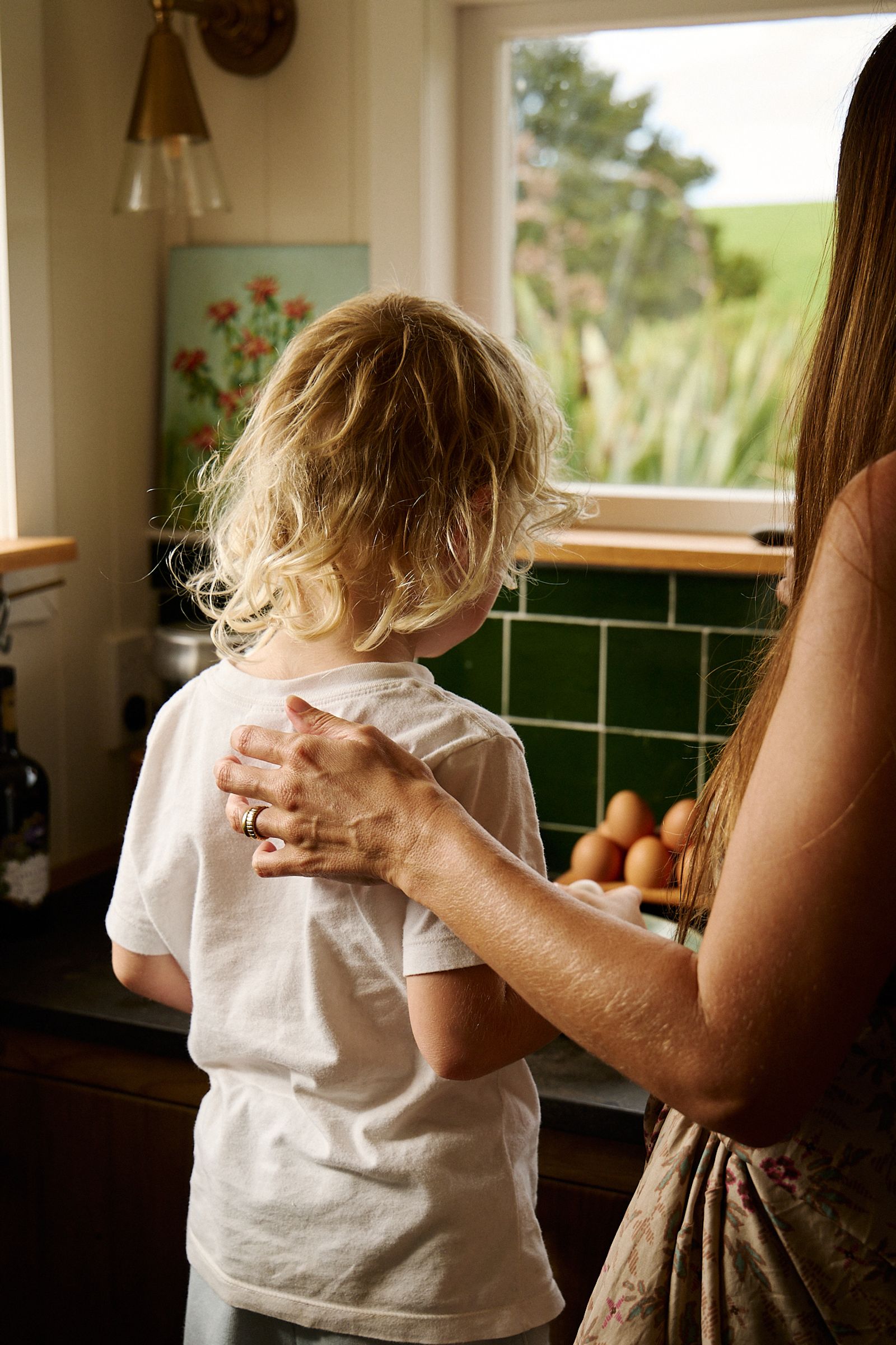 mother places hand on child's back for support in the kitchen