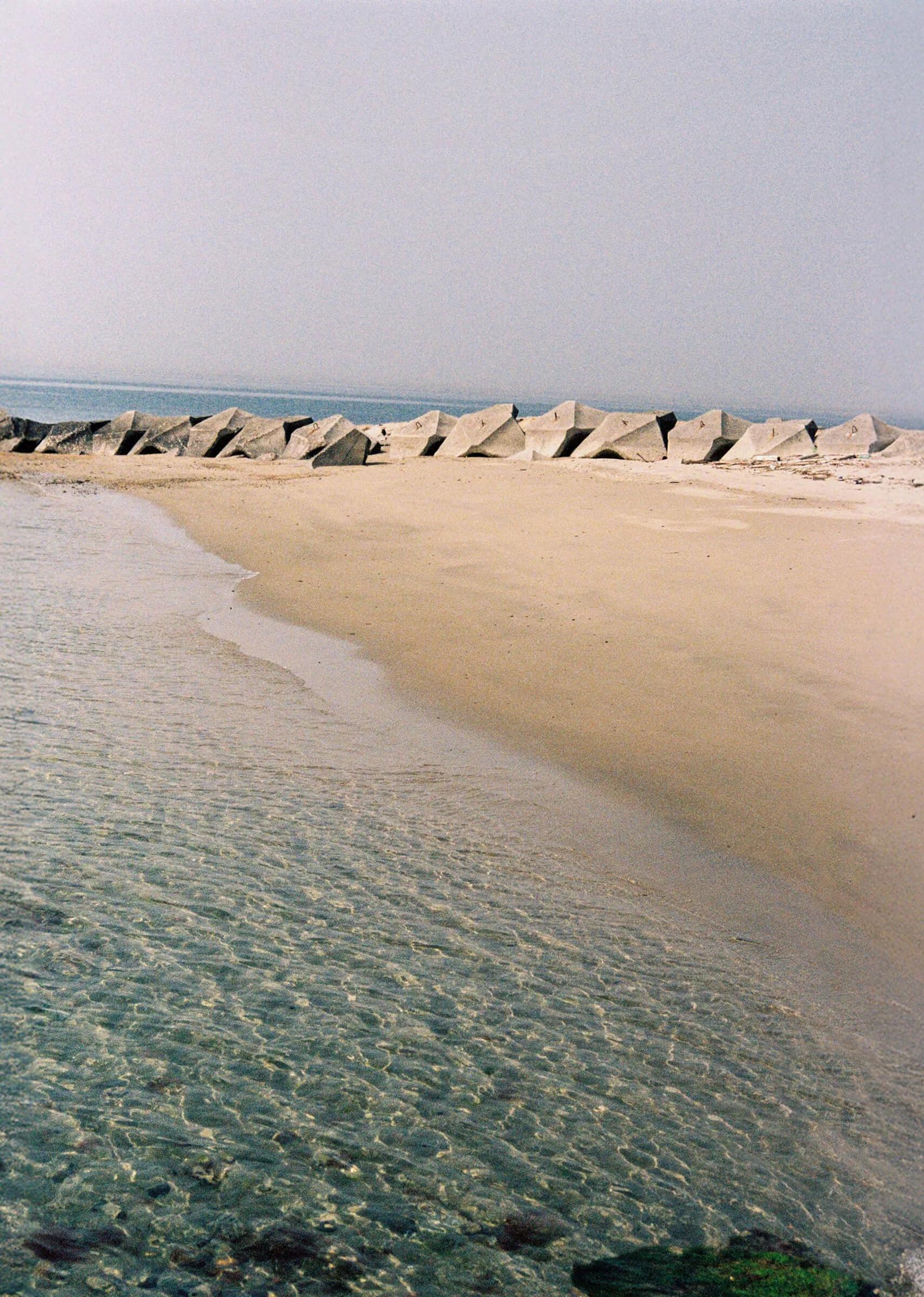 a beach with rocks in the background and clear blue water