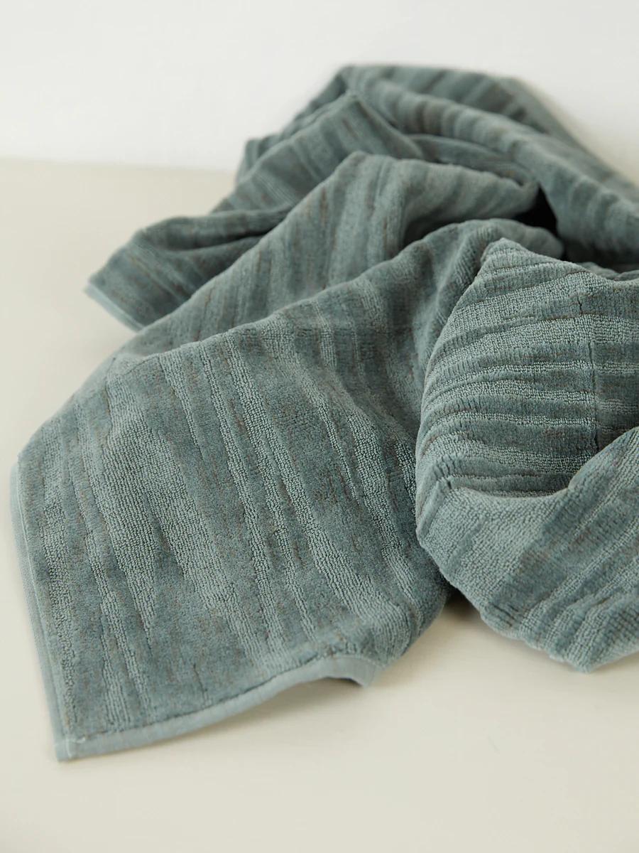 A muted green Missoni towel with a striped texture spread out on a white surface, with soft folds and creases.