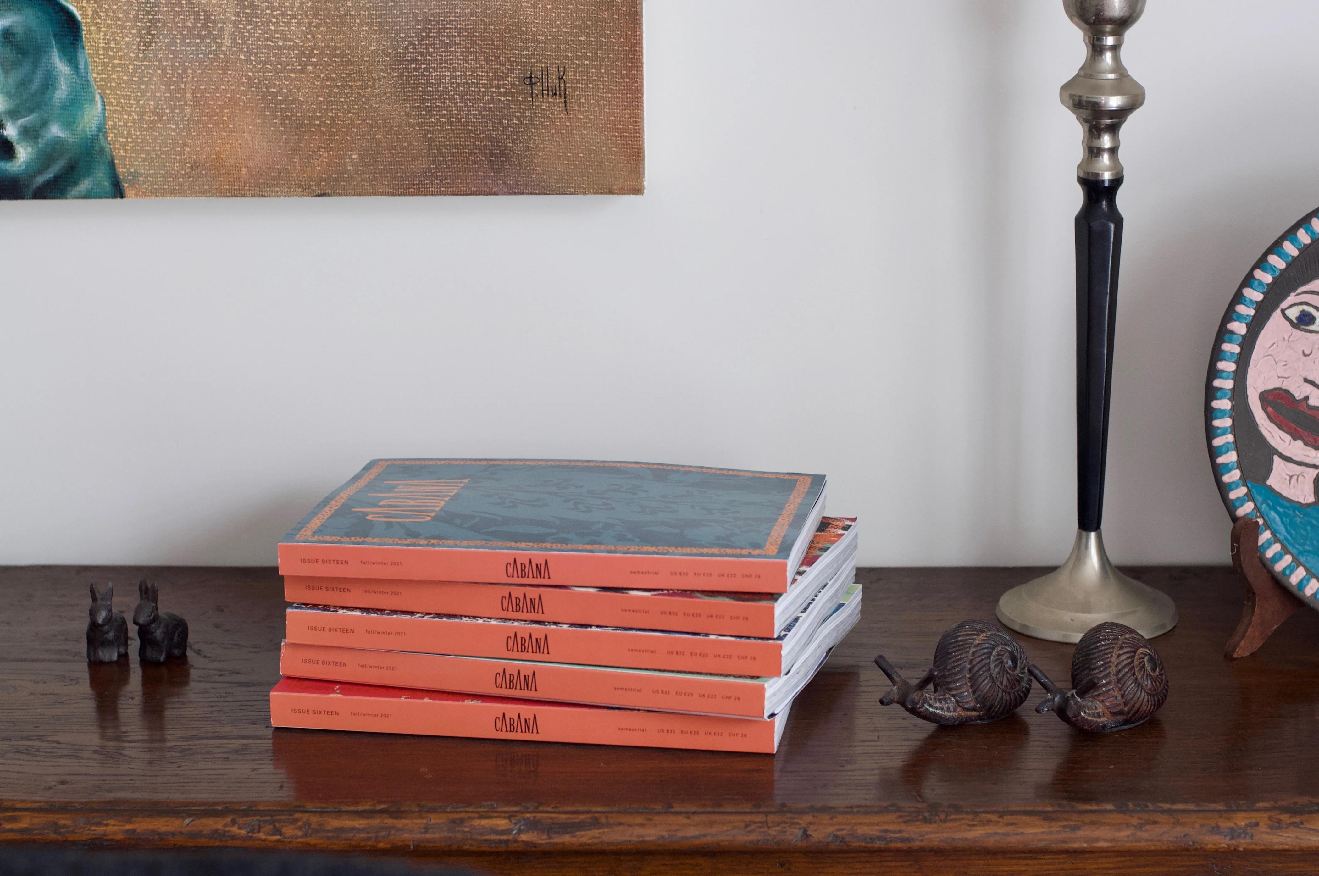 Six orange-spined books with animal figures, lamp, and ornament. Framed art above. Eclectic, cosy decor style.