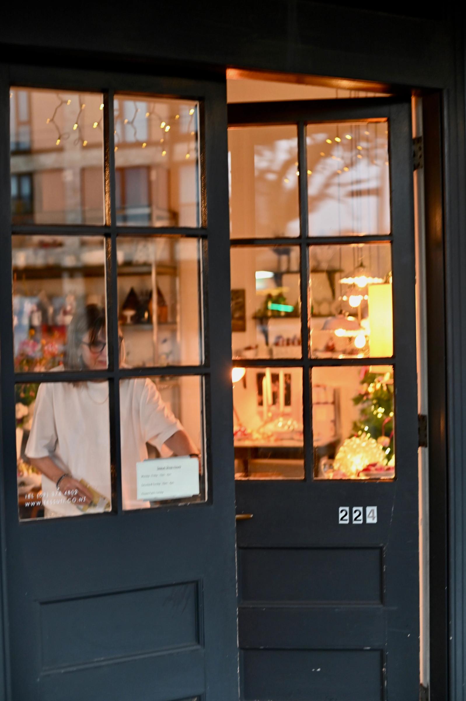 Ali closing the store door at night, store glowing with lights behind her